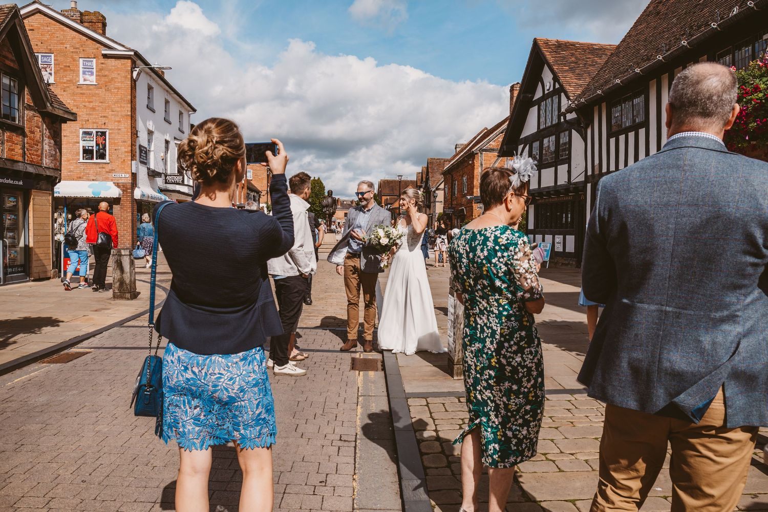 A wedding party walking down a historic Tudor-style street with timber-framed buildings in the background.