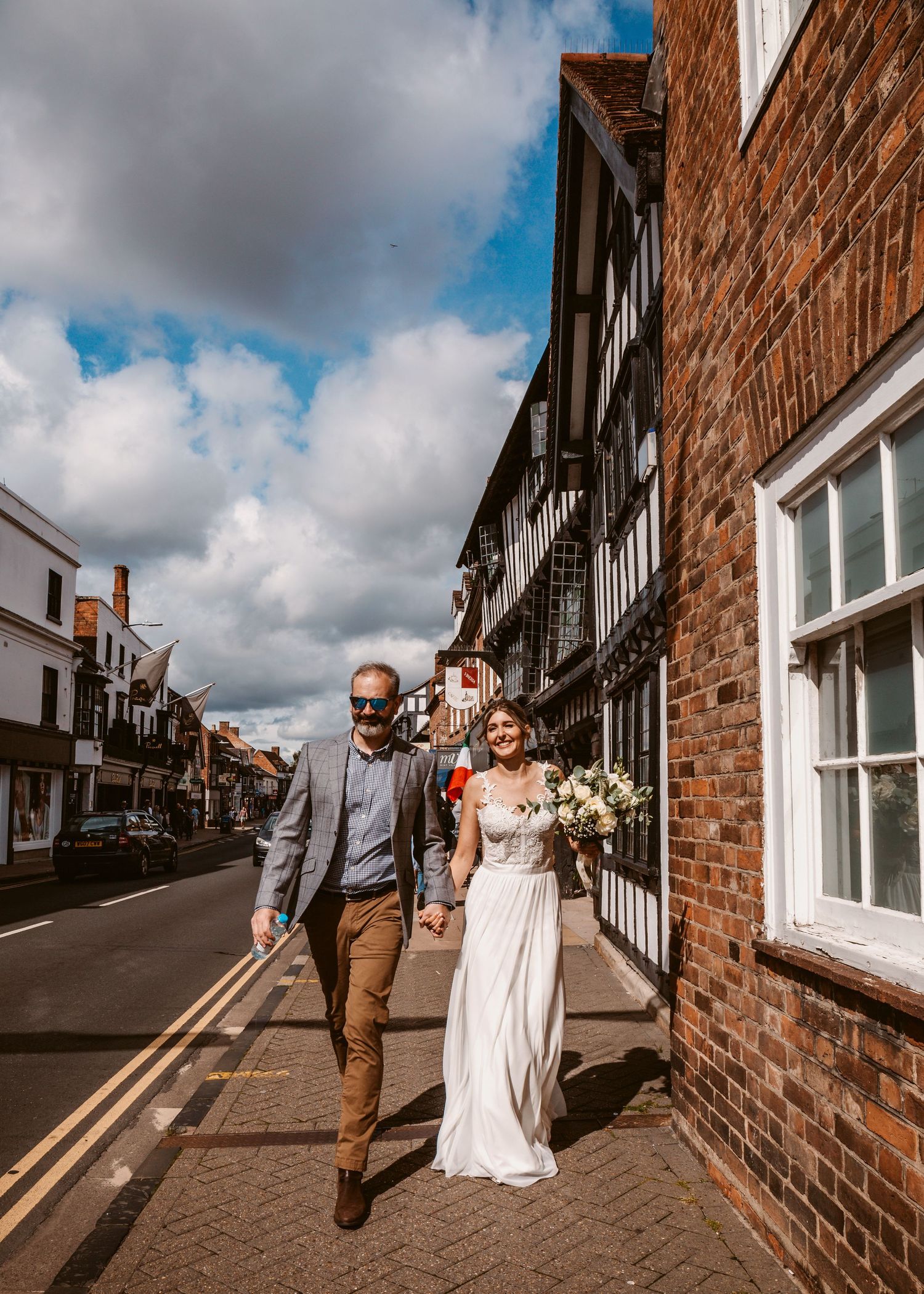 A couple strolling down a historic street lined with Tudor-style architecture and brick buildings.