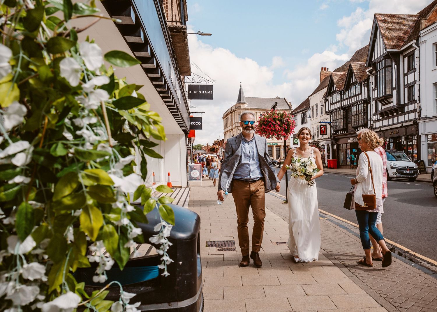 Couple strolls down charming Tudor-style village street with traditional architecture.