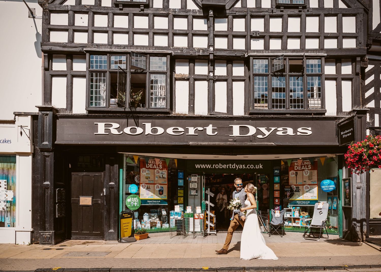 Wedding couple poses outside Robert Dyas storefront in Tudor-style building.