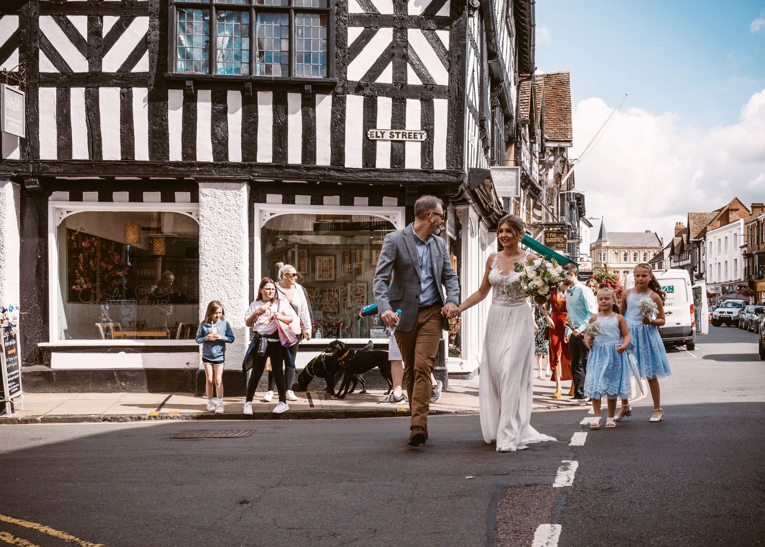 A wedding party walking through a charming Tudor town with timber-framed buildings.