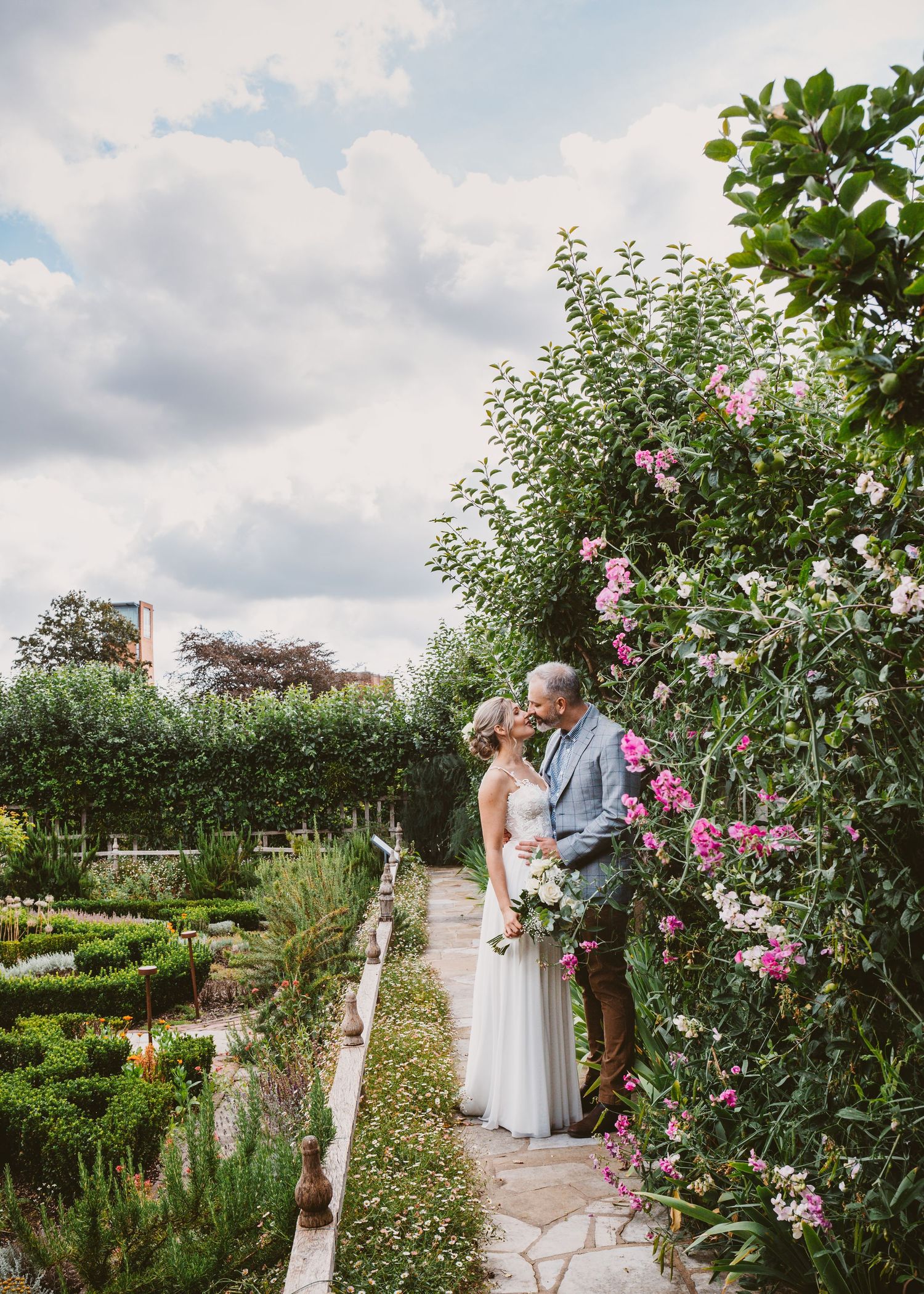A romantic moment captured in a formal garden with blooming pink roses and manicured hedges.