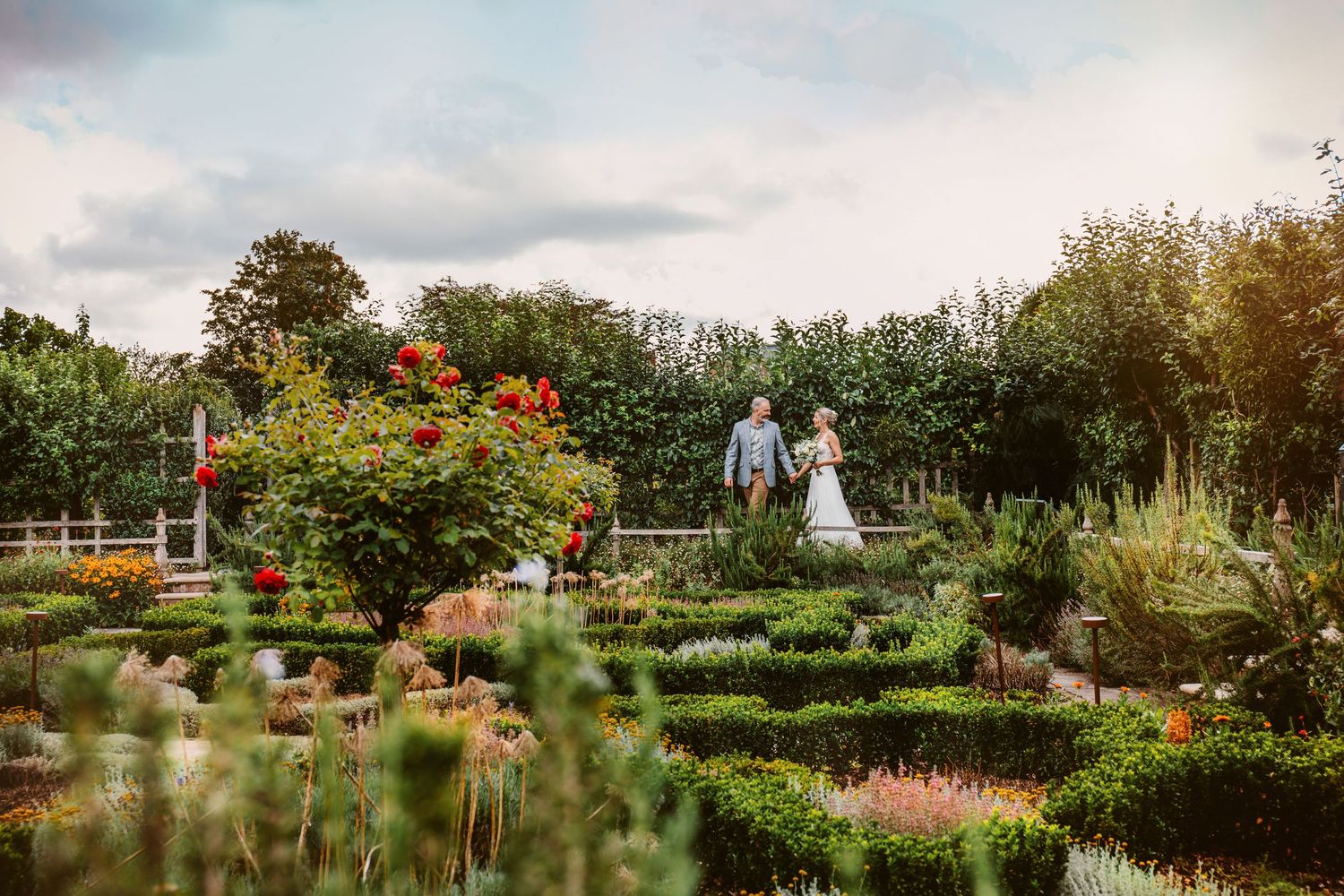 A romantic garden wedding scene with lush flowers and greenery against a cloudy evening sky.