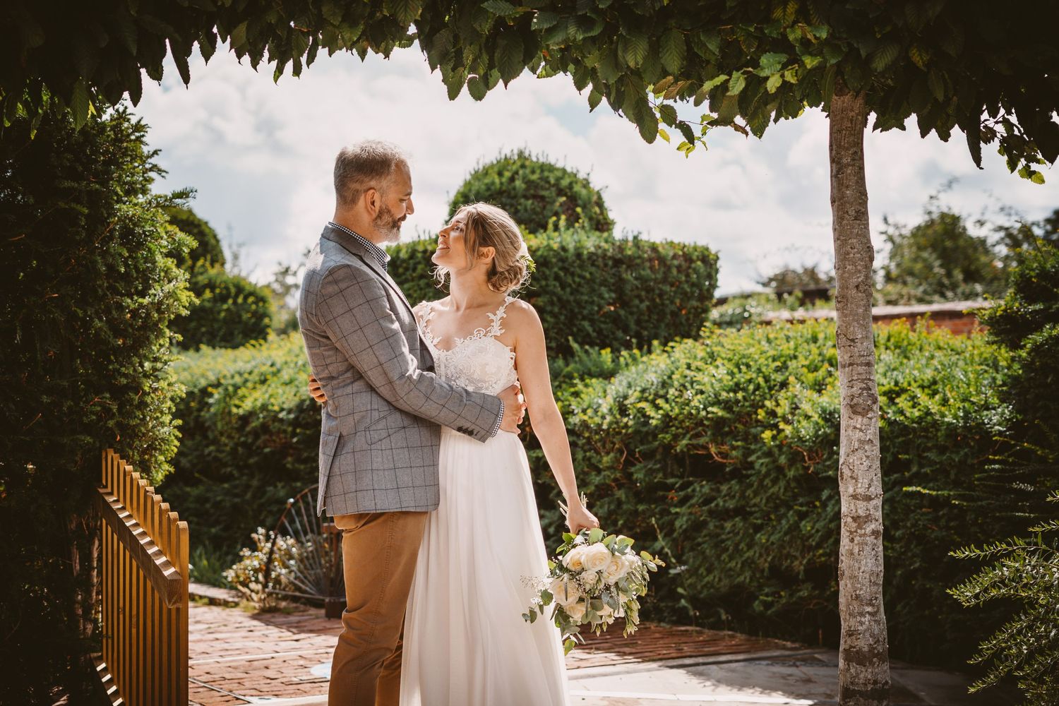 Couple poses under leafy garden arbor during wedding photoshoot.