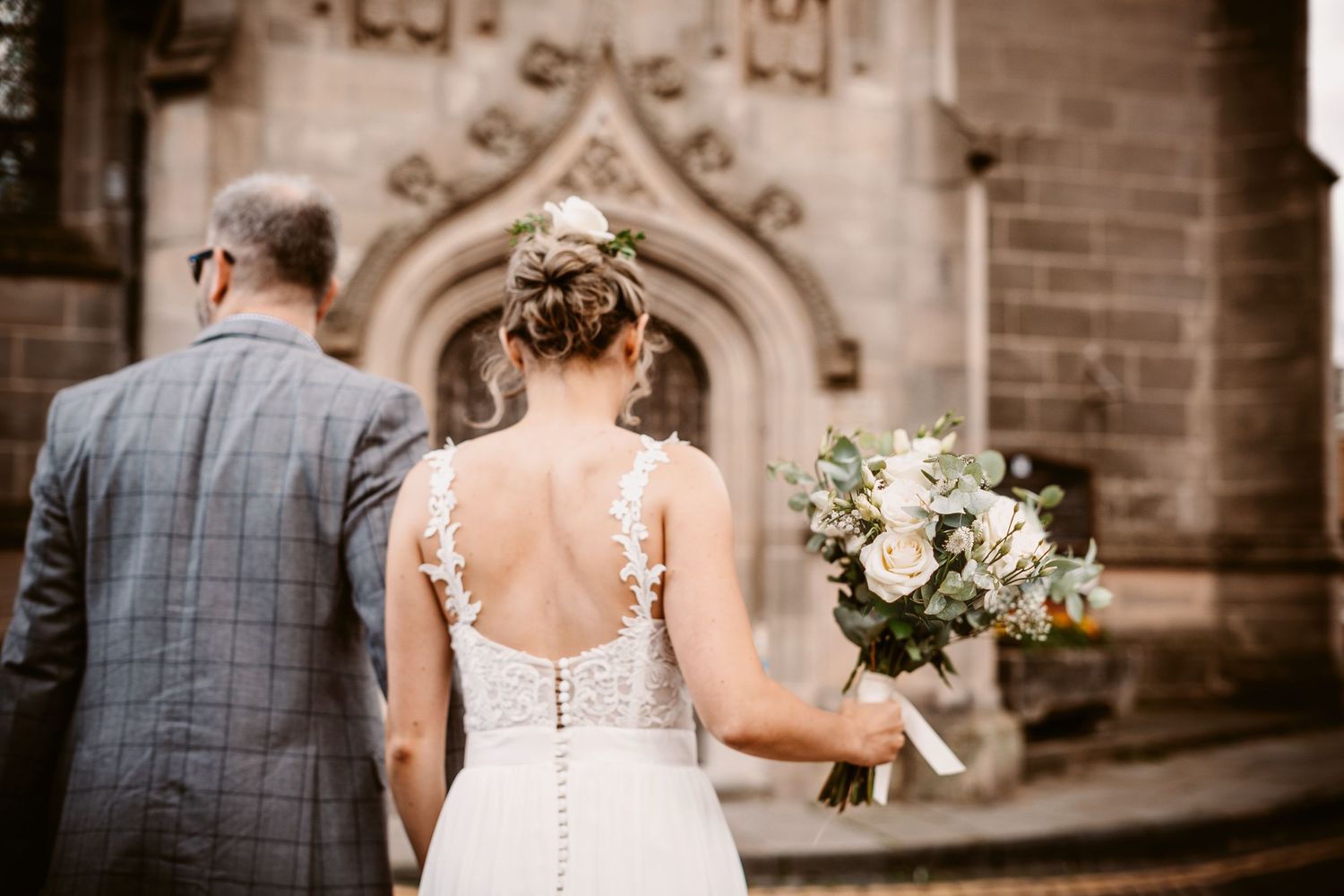 A glimpse of a wedding couple outside a gothic church entrance with a beautiful white bouquet.