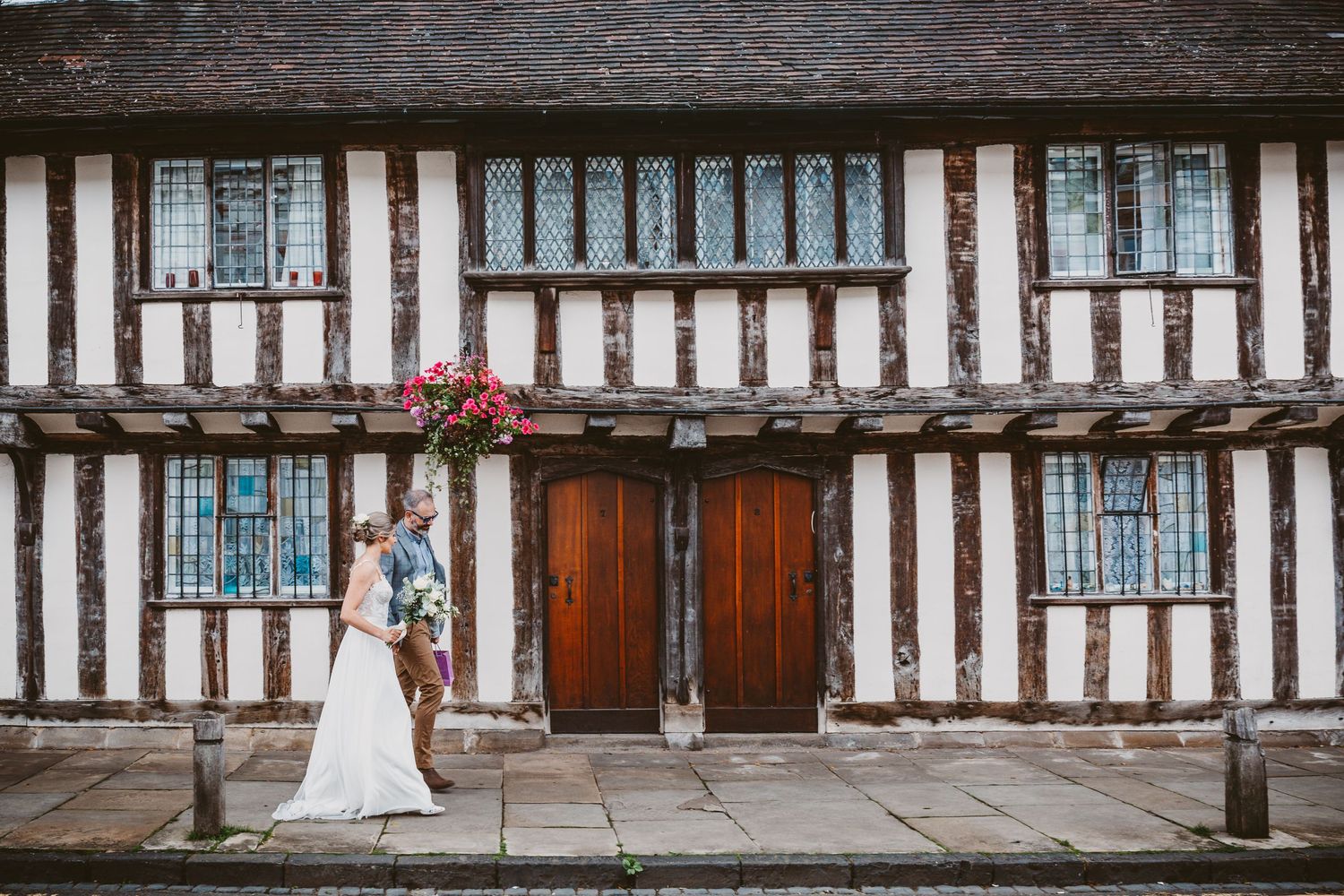 A wedding scene in front of a historic Tudor-style building with white and wood beam architecture.