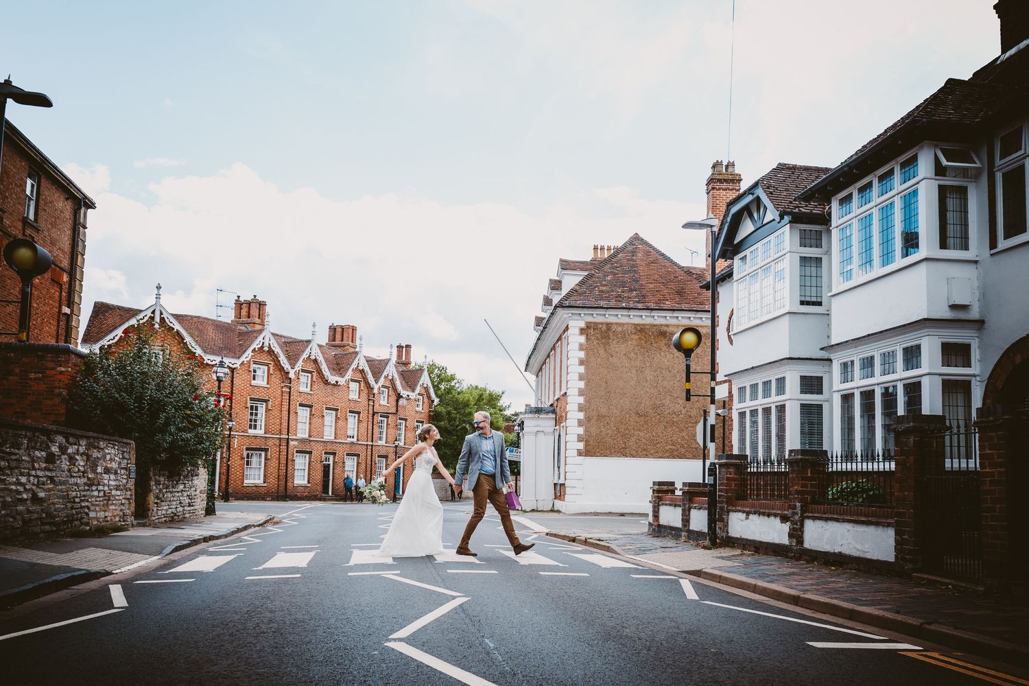 A wedding couple crossing a quaint residential street with classic British architecture in the background.
