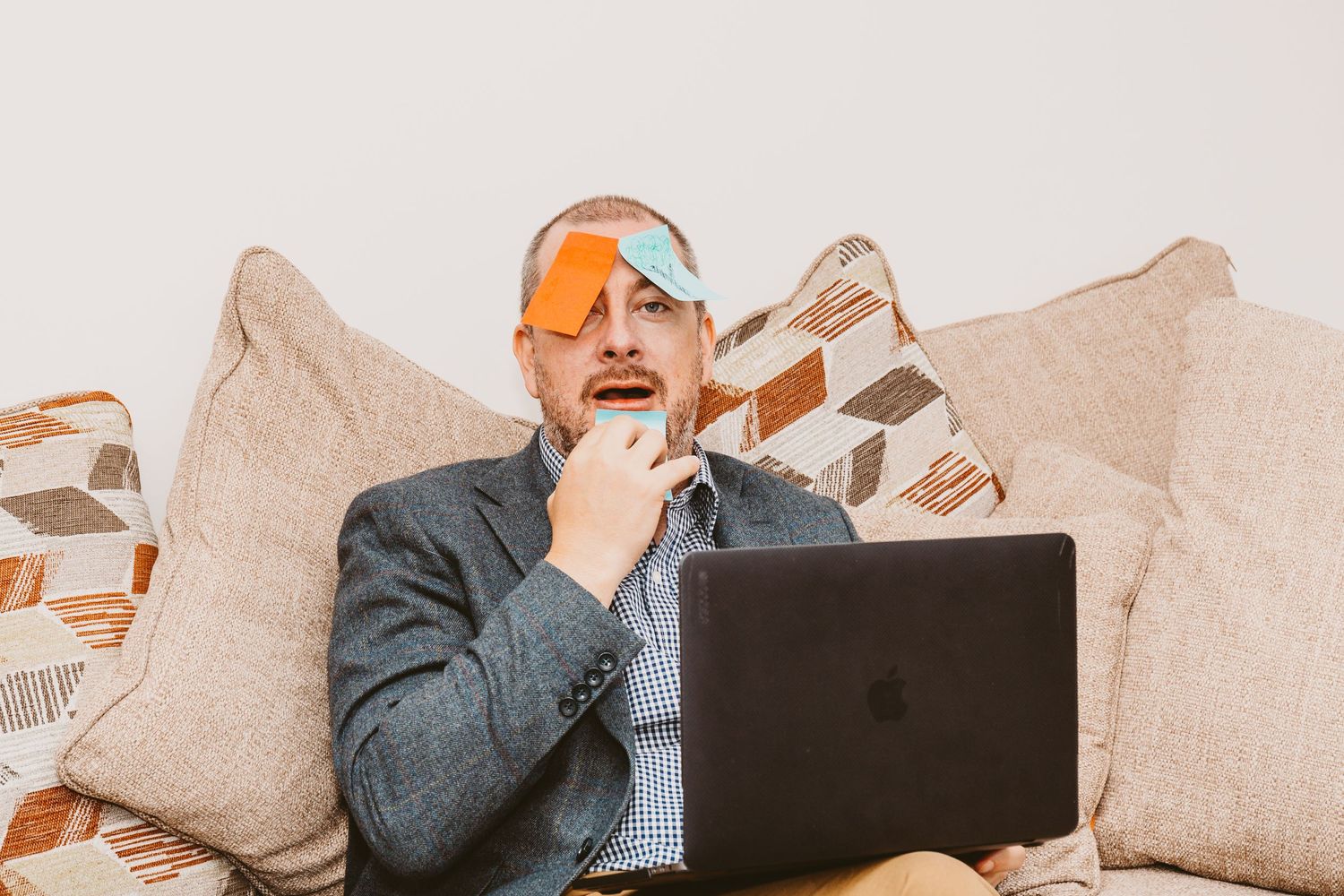 Person in suit working on laptop while sitting on couch with geometric pillows.