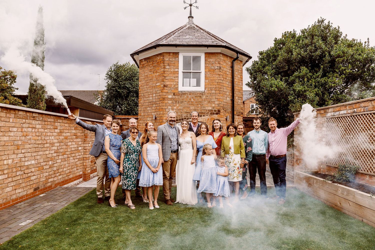 Wedding party group photo with smoke effects outside brick building.