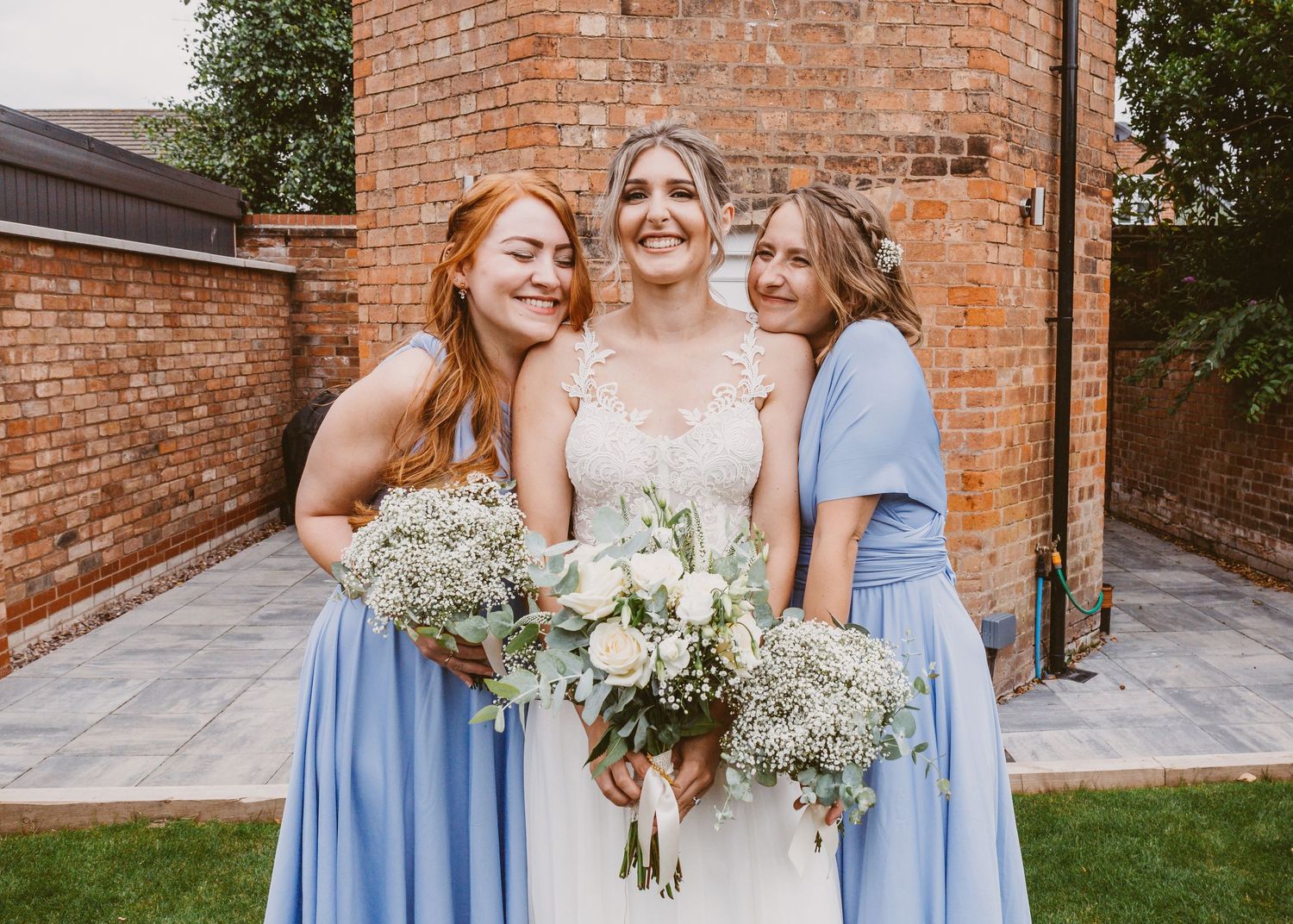 A bridal party holding bouquets against a rustic brick wall backdrop.