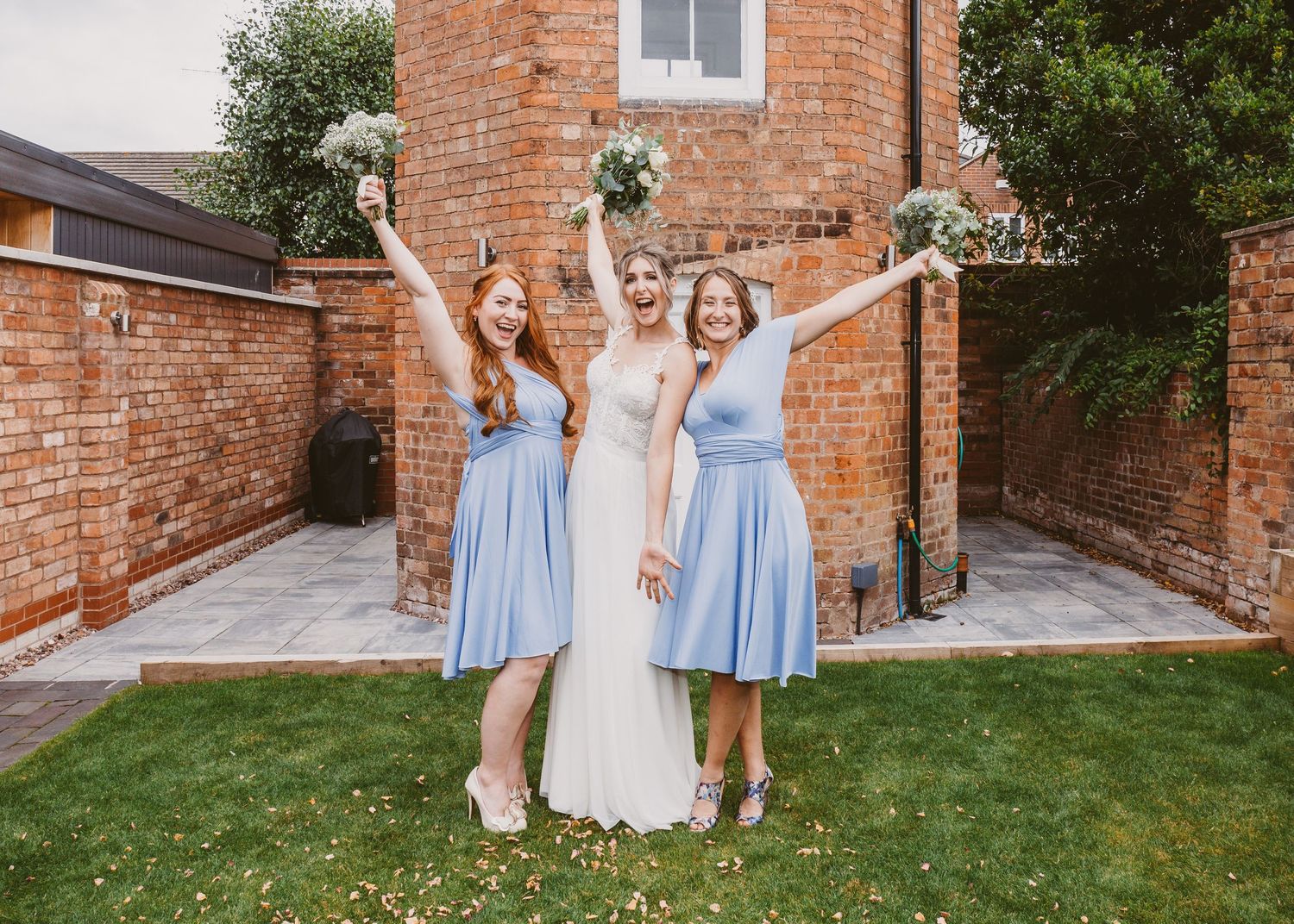 Three women in coordinated dresses celebrating joyfully in a garden setting.