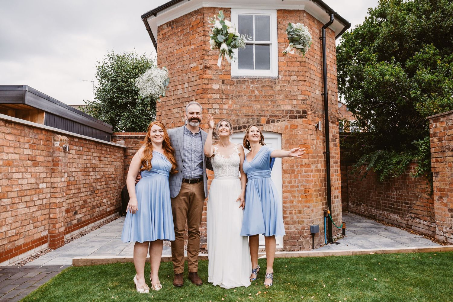 Wedding party poses in front of rustic brick building with bridesmaids in light blue dresses.