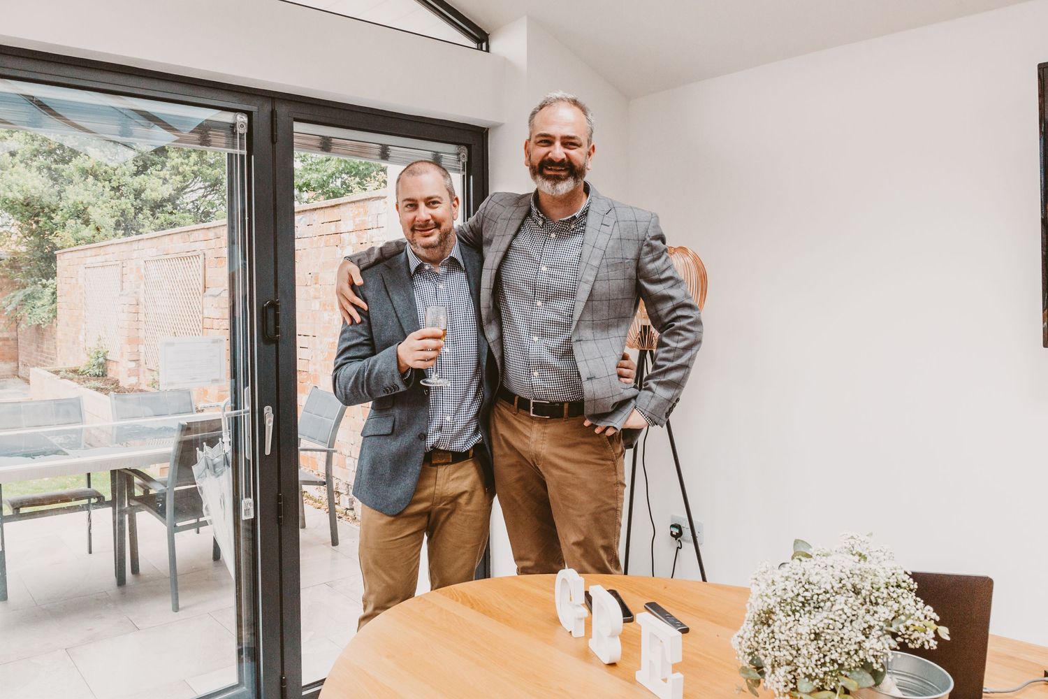 Two wedding guests sharing a moment by glass doors in an indoor reception space.