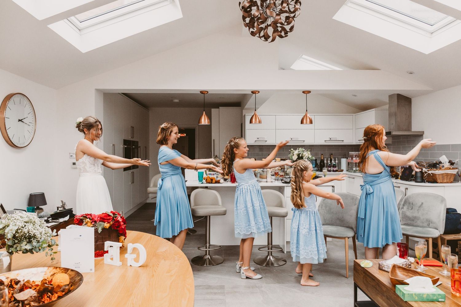 Wedding celebration scene with bridesmaids in light blue dresses preparing food in a modern kitchen.