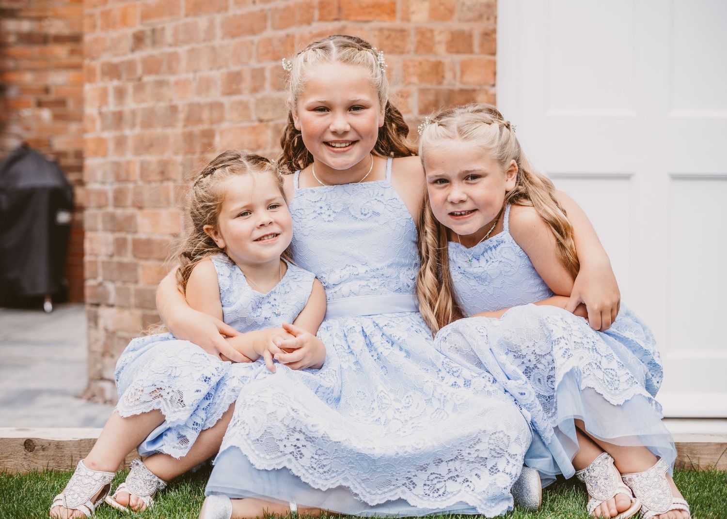 Three young girls in matching blue dresses sit together on brick steps.