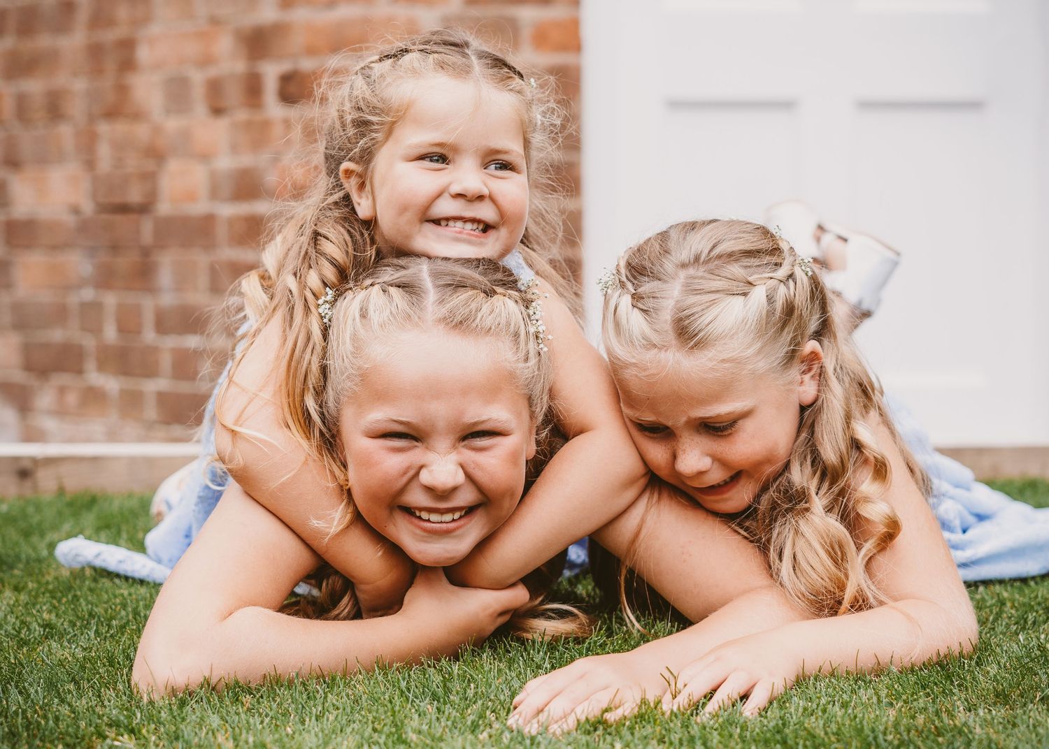 Three children playing and laughing together while laying on grass.