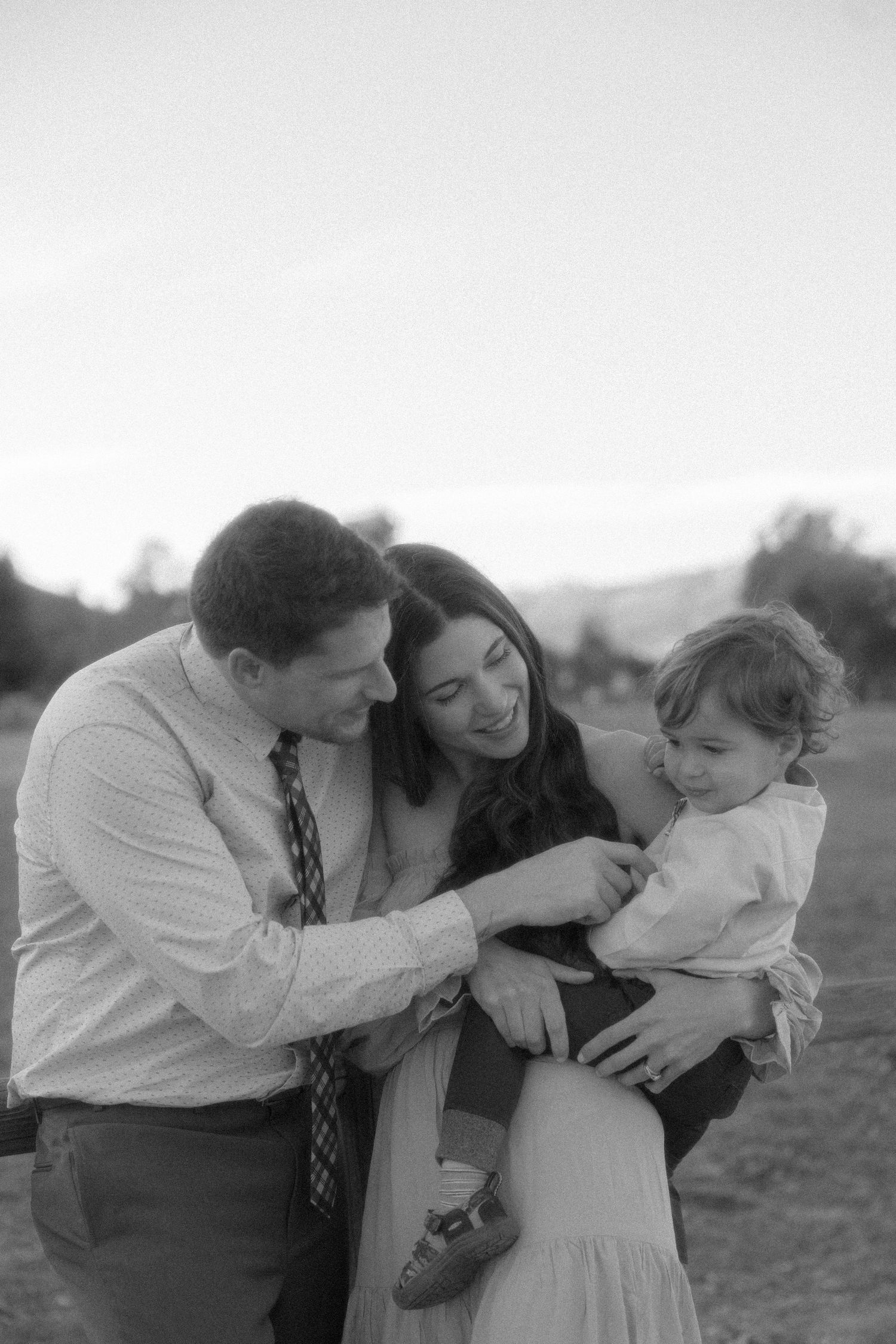 A tender black and white family moment captured outdoors in natural lighting.