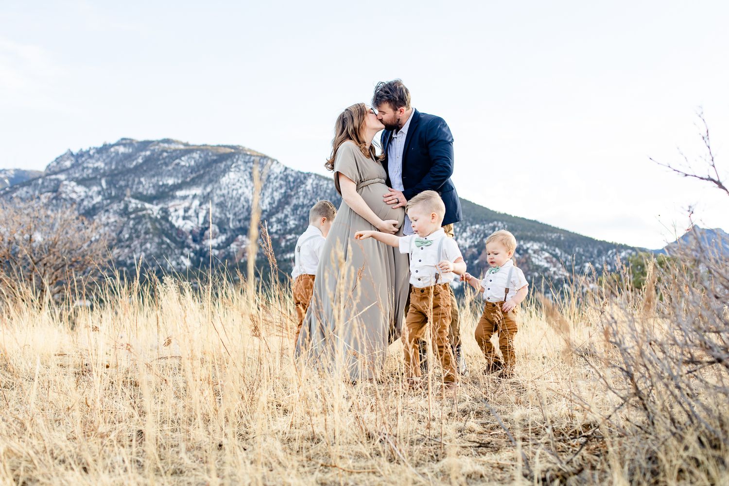 Expectant mom of three boys kisses her husband as her sons play around them in Colorado Springs, Colorado.