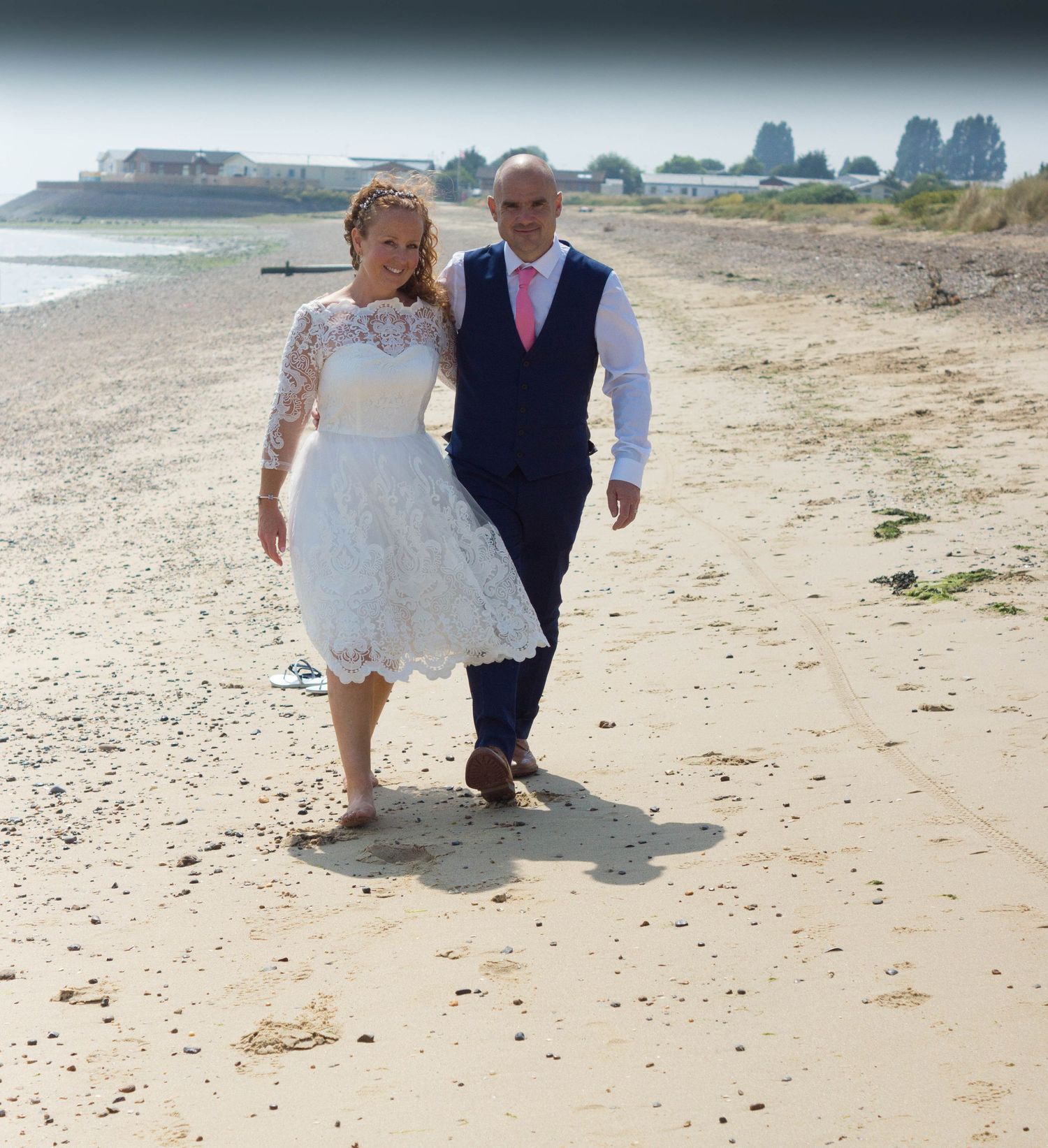 A couple takes a romantic walk along a sandy beach in wedding attire.