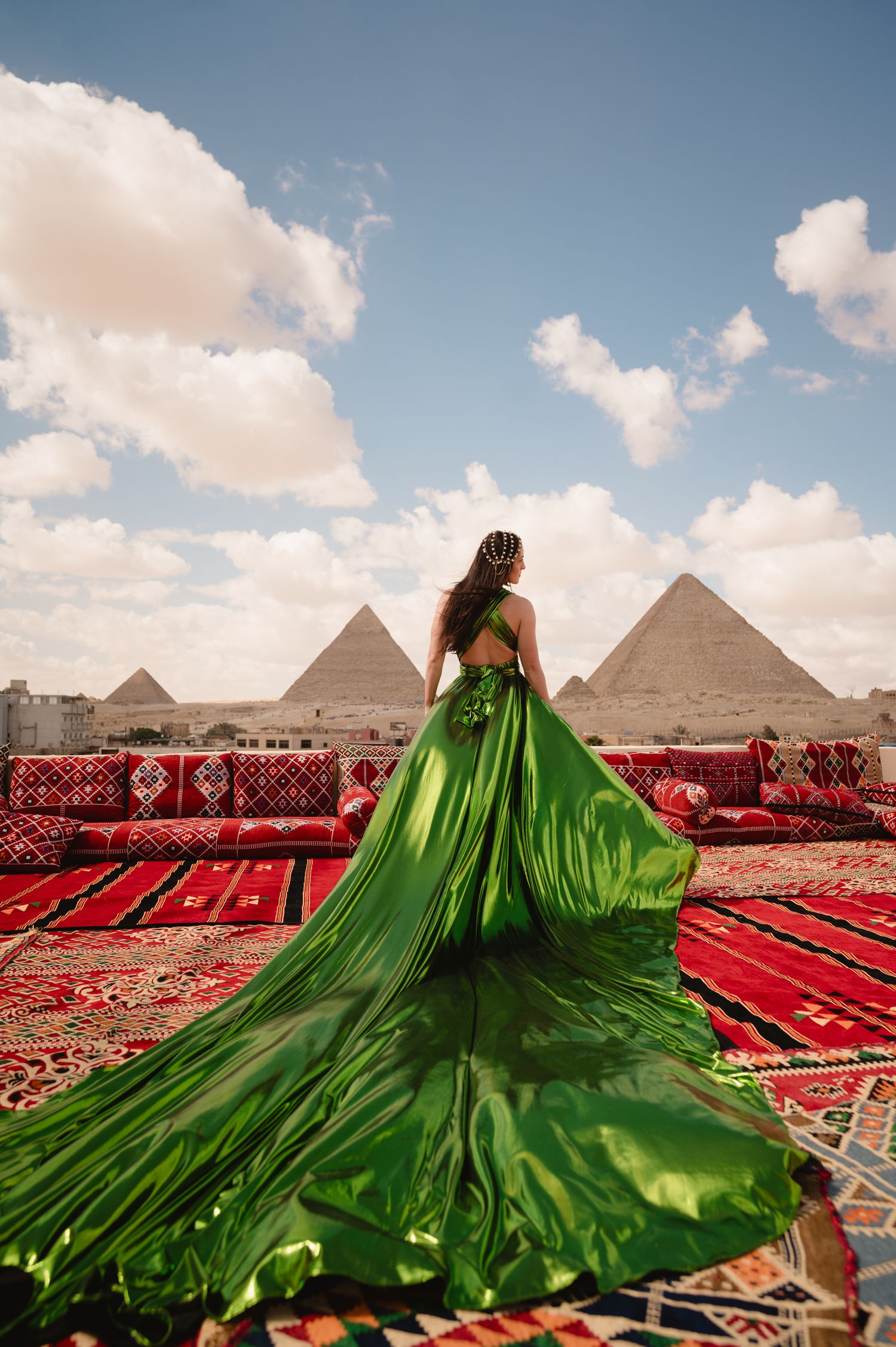 A flowing green dress billows dramatically against red carpets with the iconic pyramids of Giza in the background.