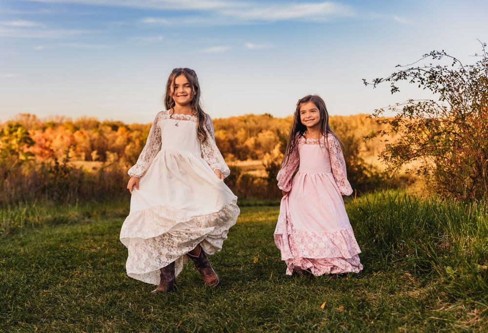 Children in flowing dresses twirling in a sunlit field during golden hour.