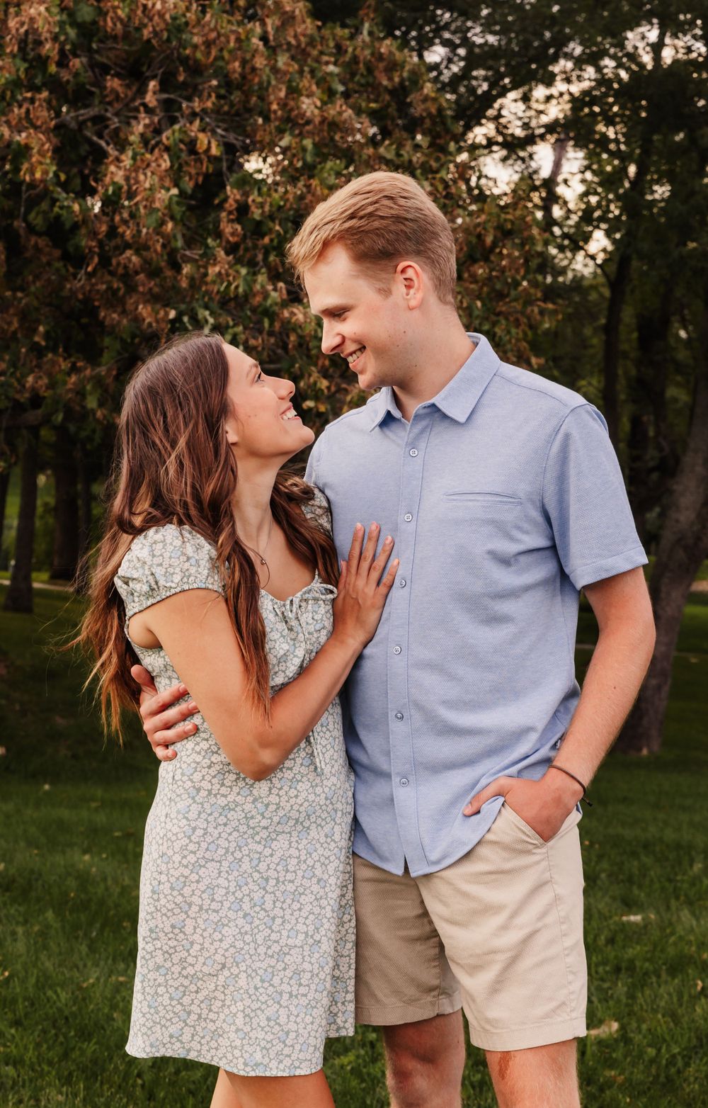 Couple sharing intimate moments in a park during golden hour wearing casual summer outfits.