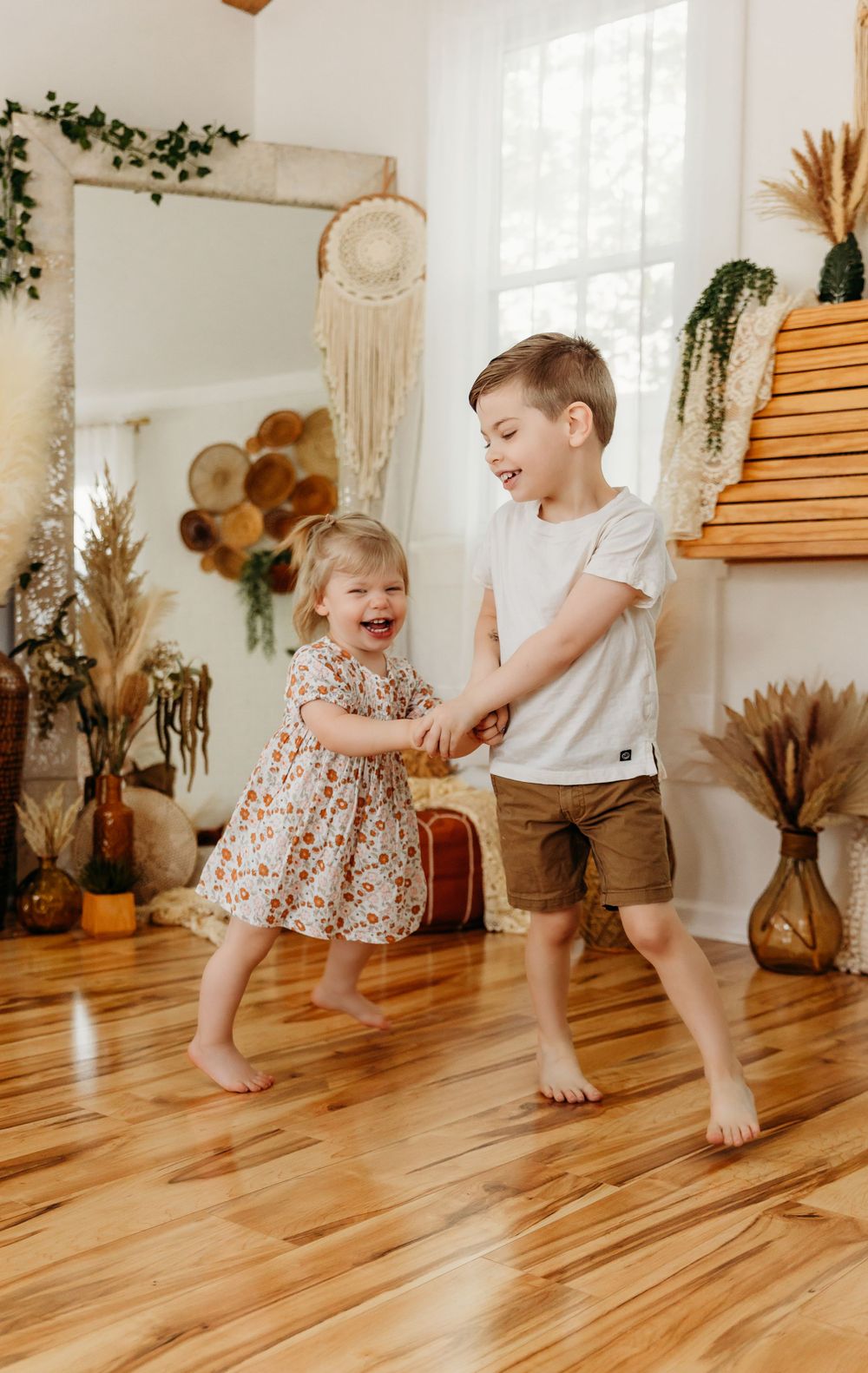 Children playing and laughing on hardwood floors in a bright, naturally lit room with indoor plants.