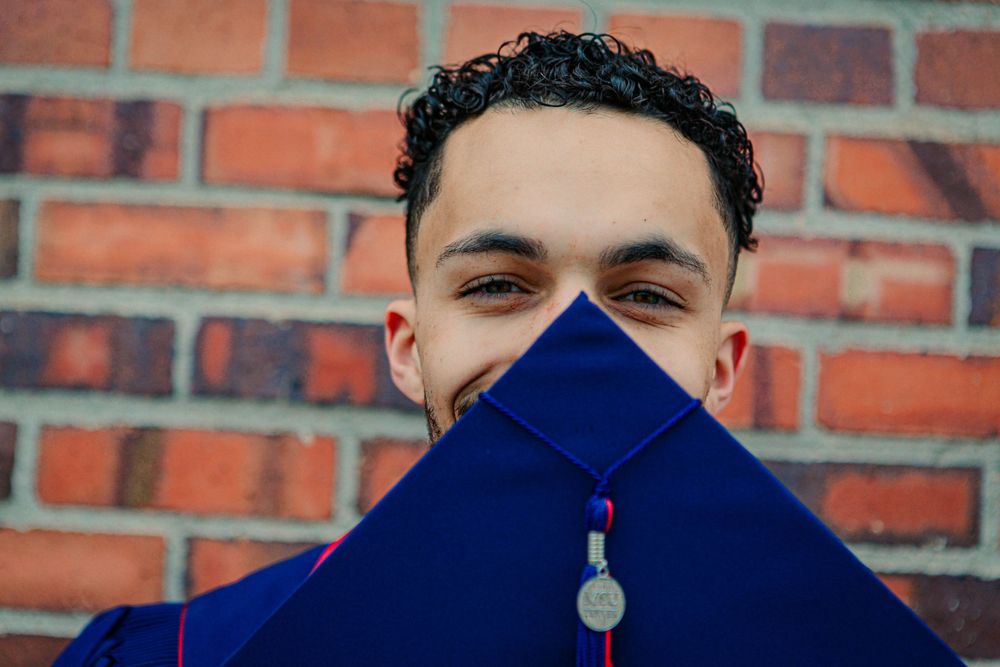 A close-up shot of a graduation cap and tassel against a brick wall background.