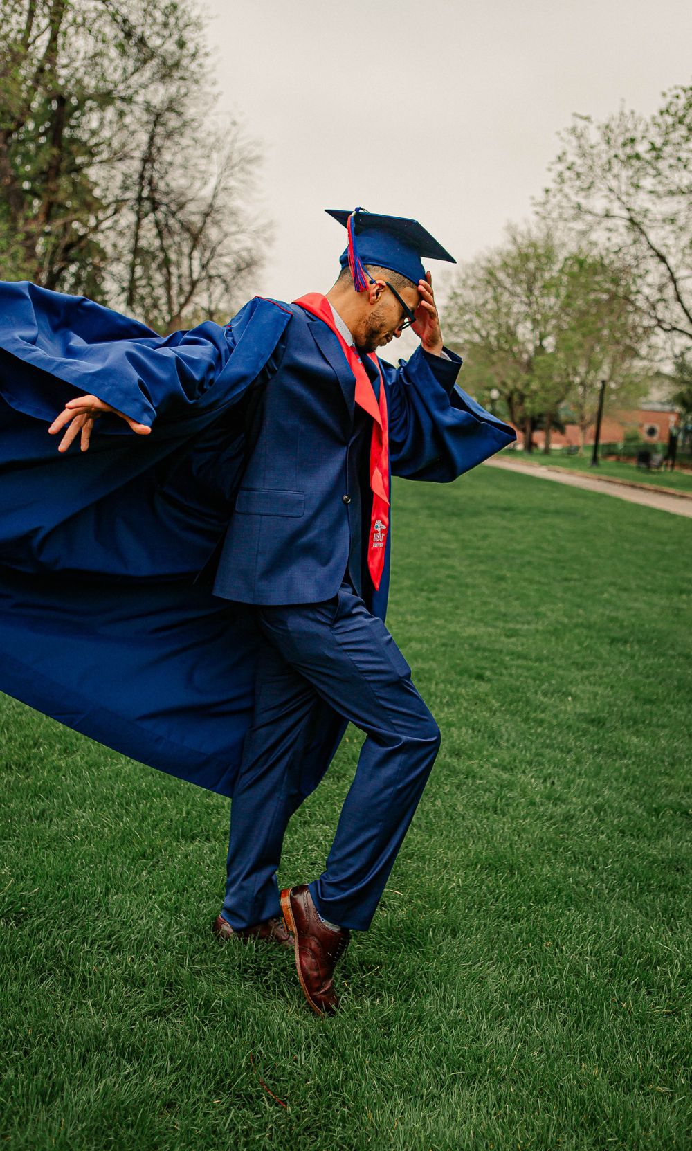 Graduate in blue gown striking dynamic pose on grass with flowing robe.