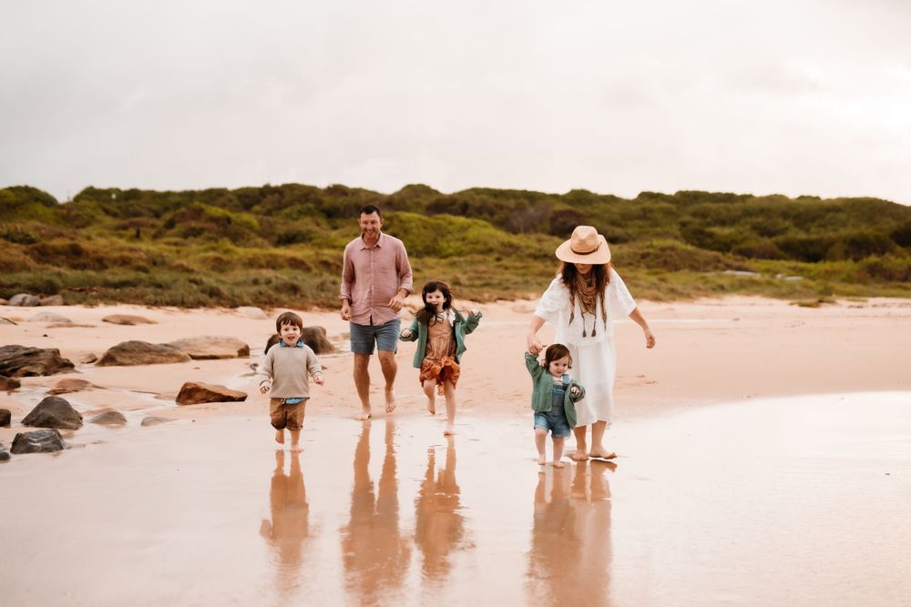 A family walks together along a scenic beach shoreline with sand dunes in the background during golden hour.