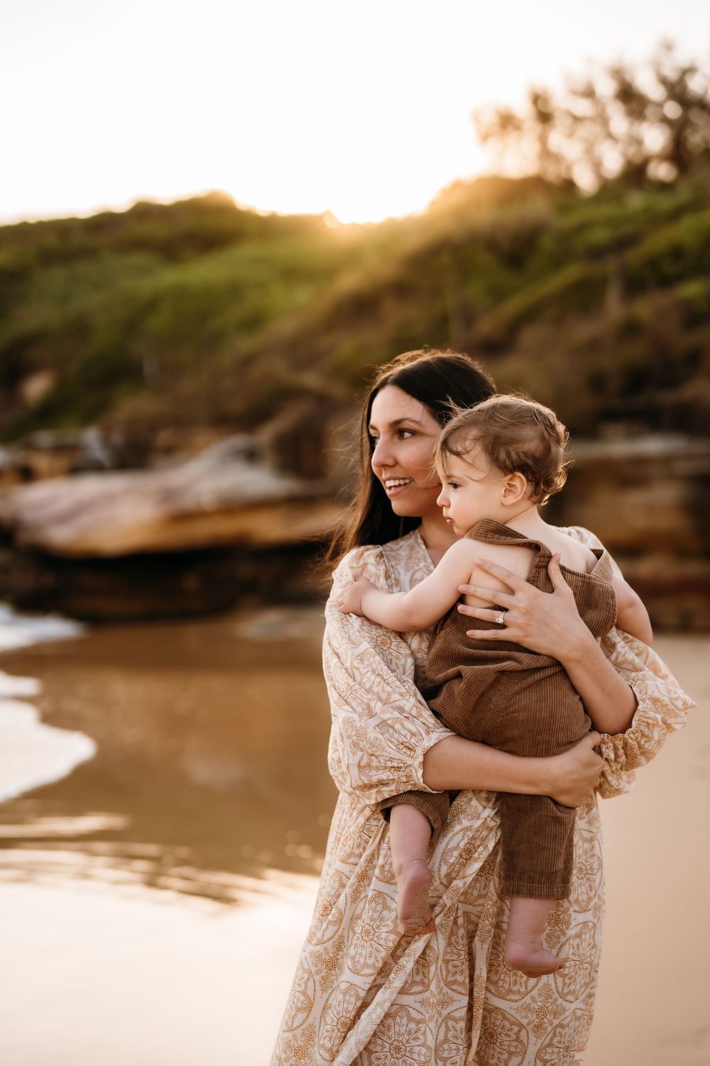 A mother and child share tender embraces on a beach at sunset with golden light illuminating their special moments.