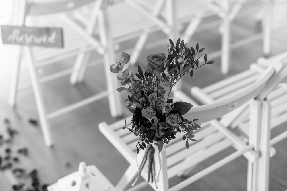 White chairs arranged in rows with flower bouquets adorning the aisle at an outdoor wedding ceremony.