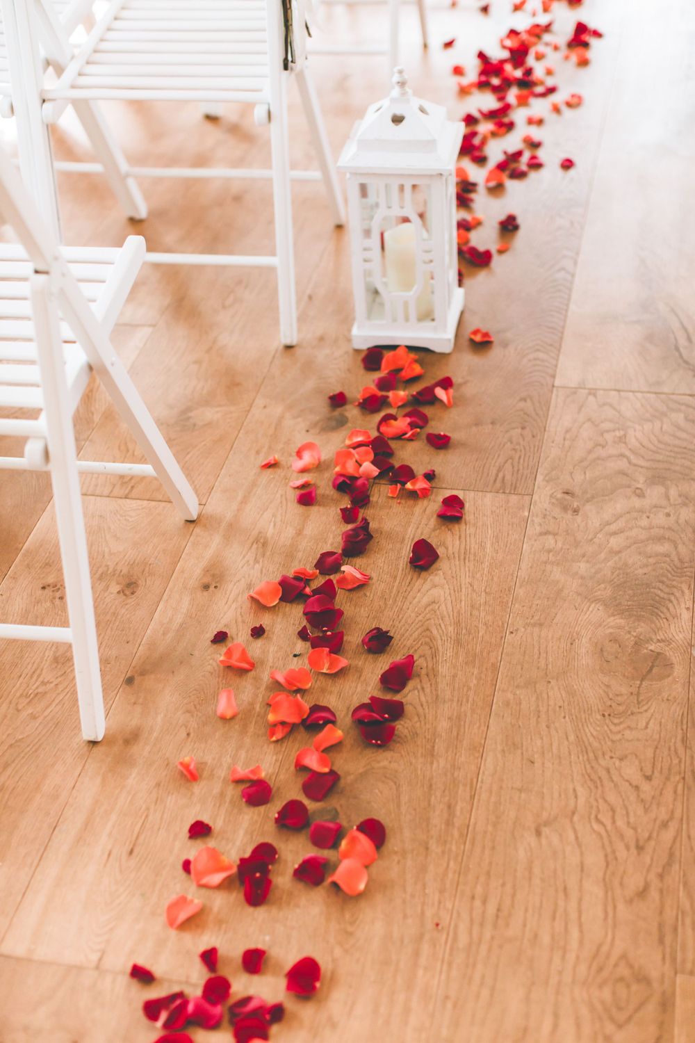 Red rose petals scattered elegantly across a wooden floor create a romantic path at a wedding venue.