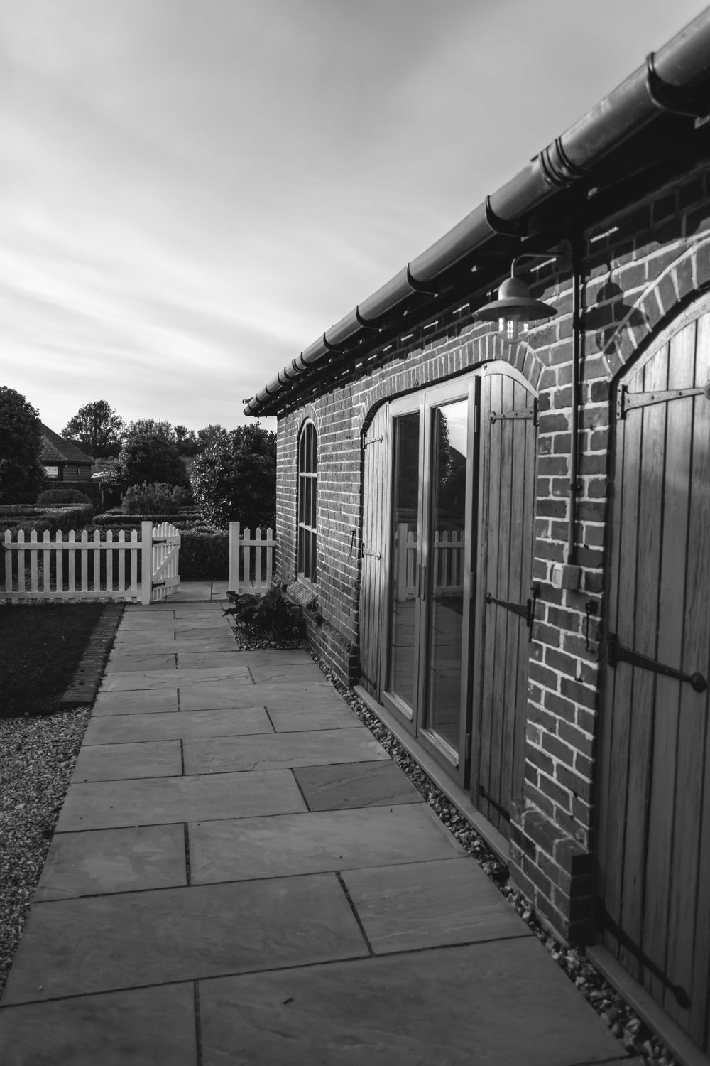 Black and white exterior view of brick building with stone pathway and wooden shutters.