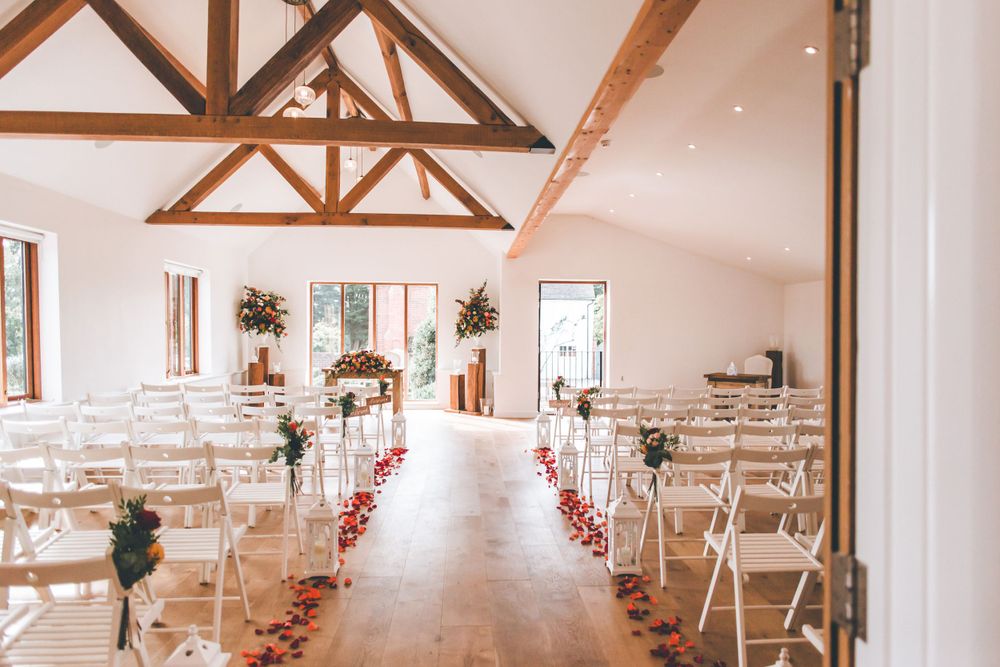 Indoor wedding ceremony space with wooden beams and white chairs lined with rose petals.