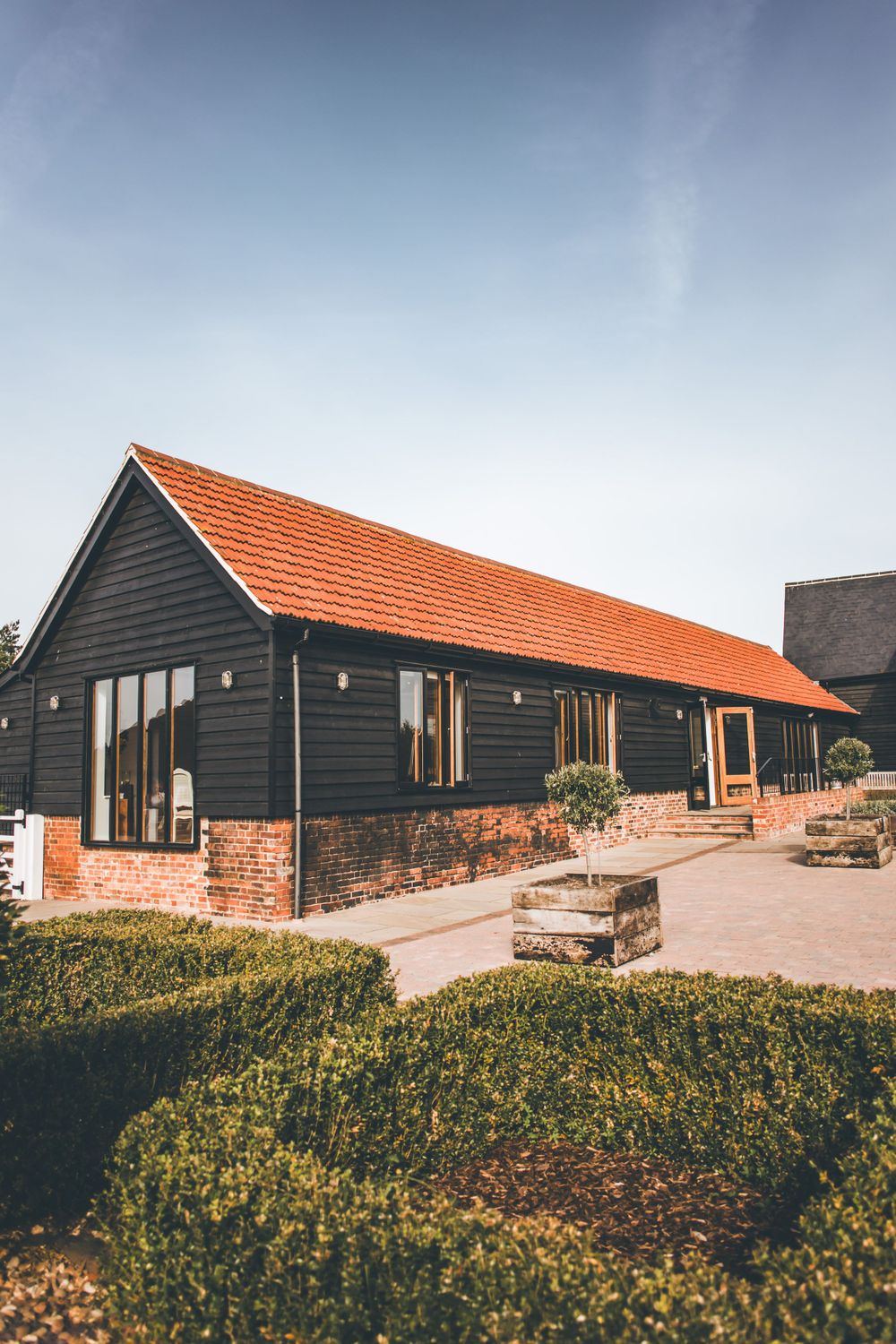 Modern black barn-style venue with orange roof and brick foundation surrounded by landscaping.