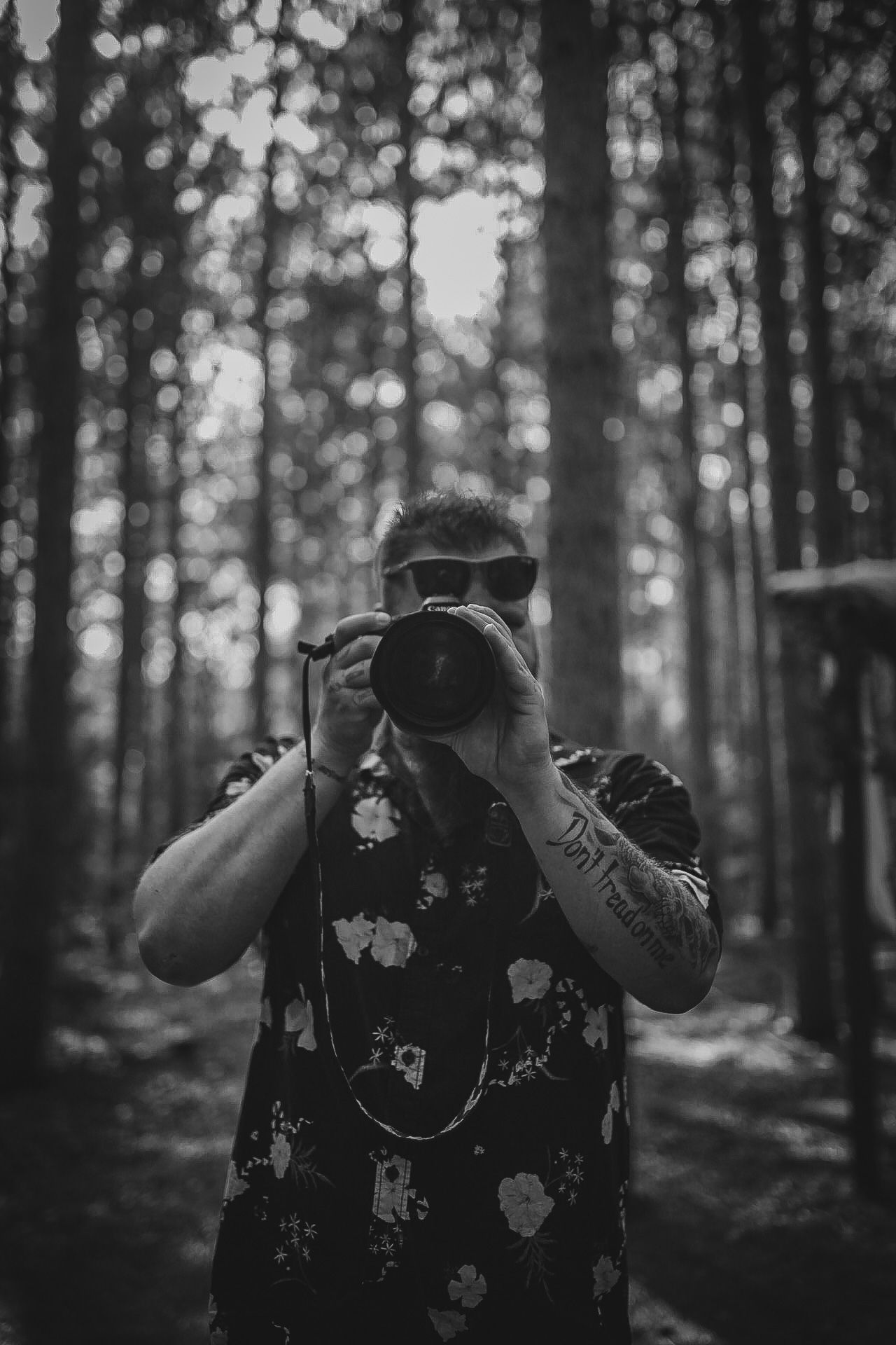 Black and white portrait of photographer taking picture in forest with bokeh background.