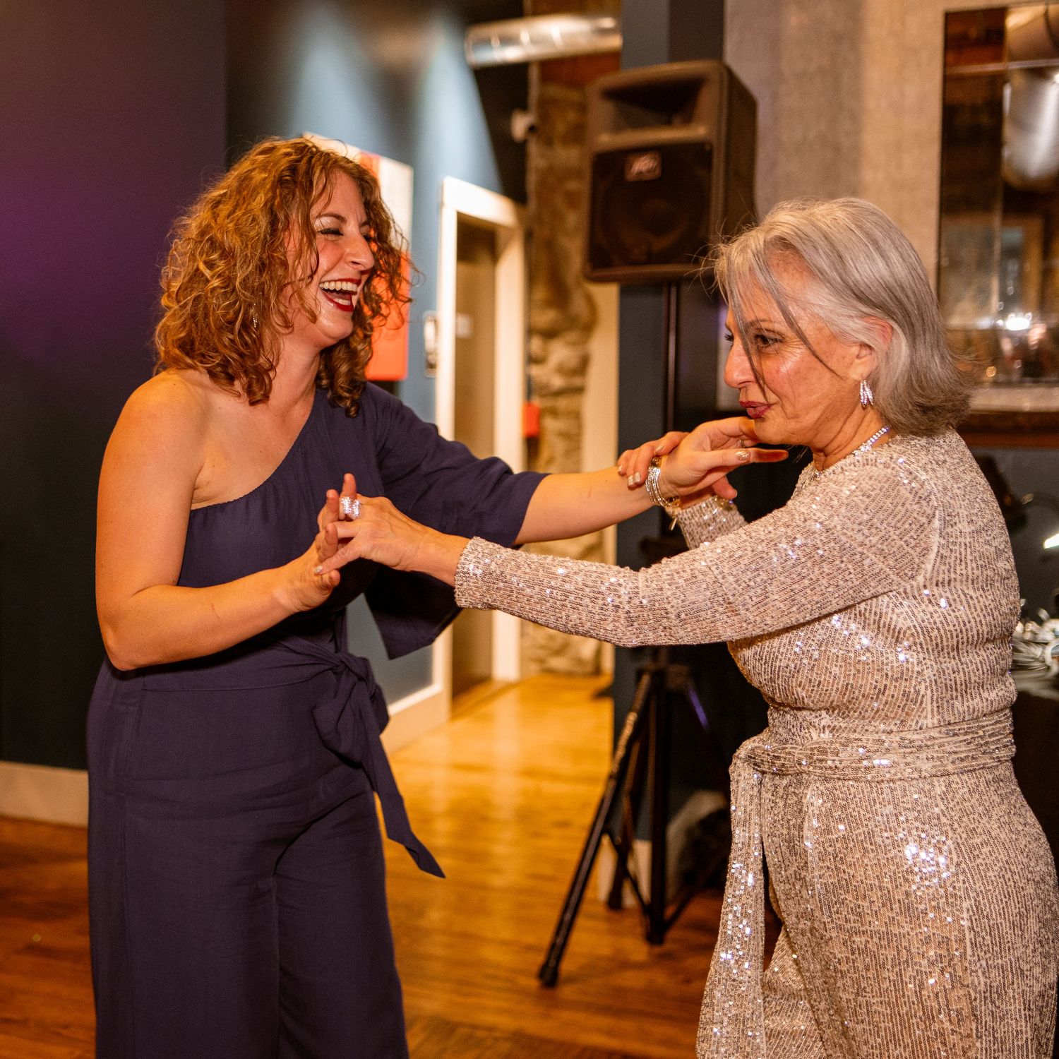 Two women sharing a joyful dance moment in formal attire at an indoor venue.