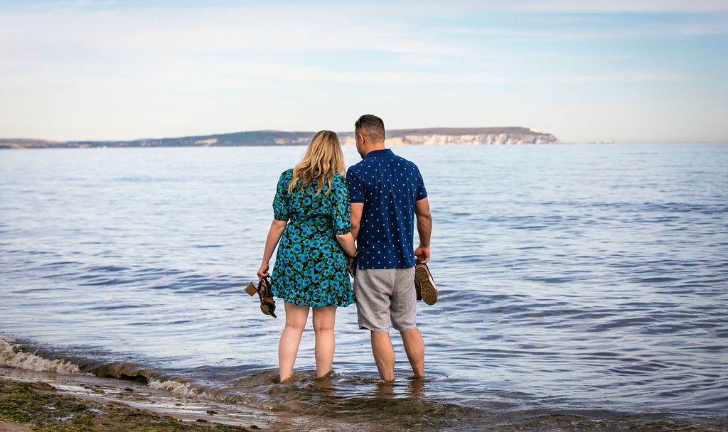 A couple stands at the ocean's edge looking out at distant cliffs while wearing coordinated blue outfits.