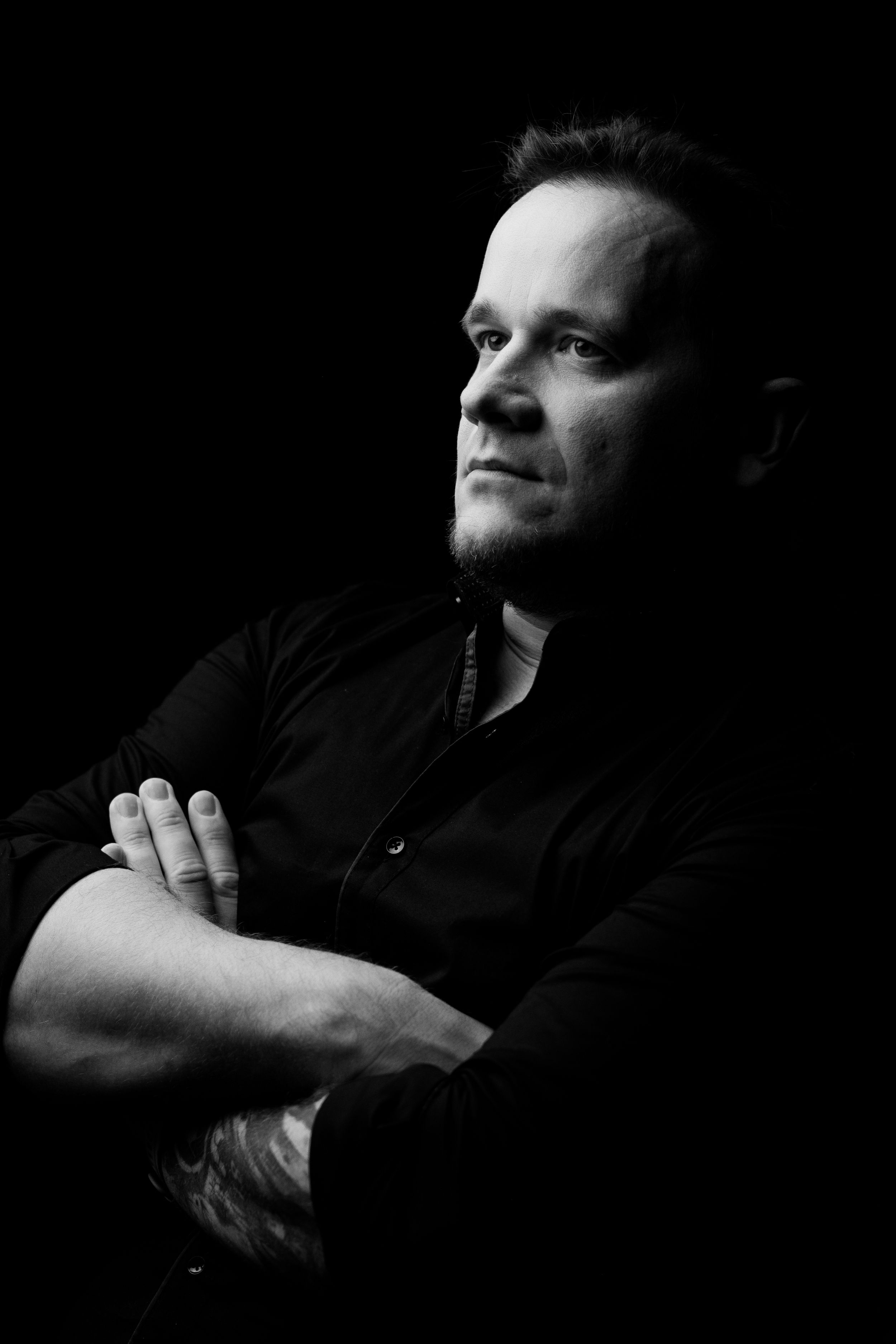 Moody low-key portrait of a person in black clothing against dark background.