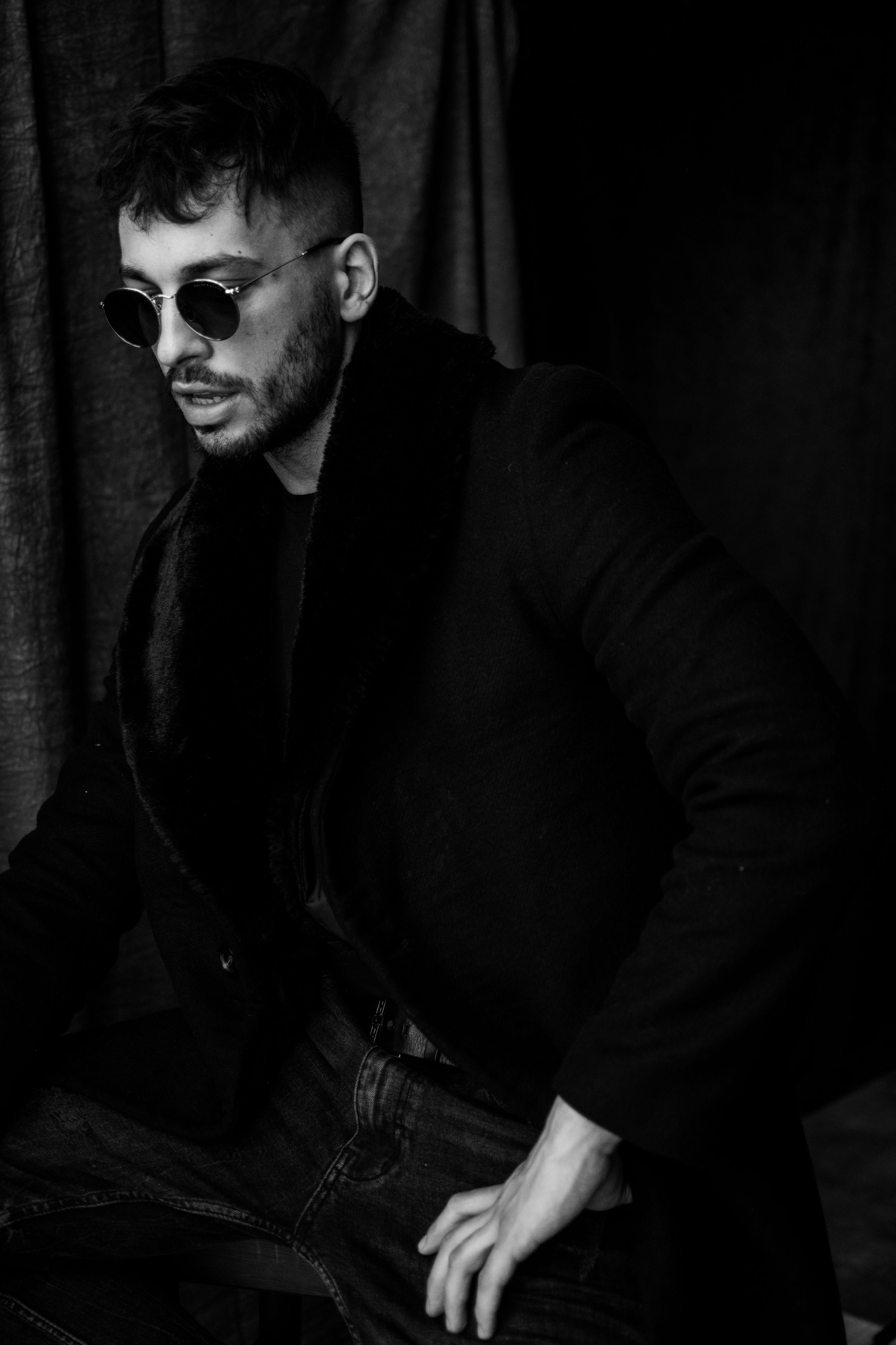 Stylish portrait of a person wearing sunglasses and black jacket in moody lighting.