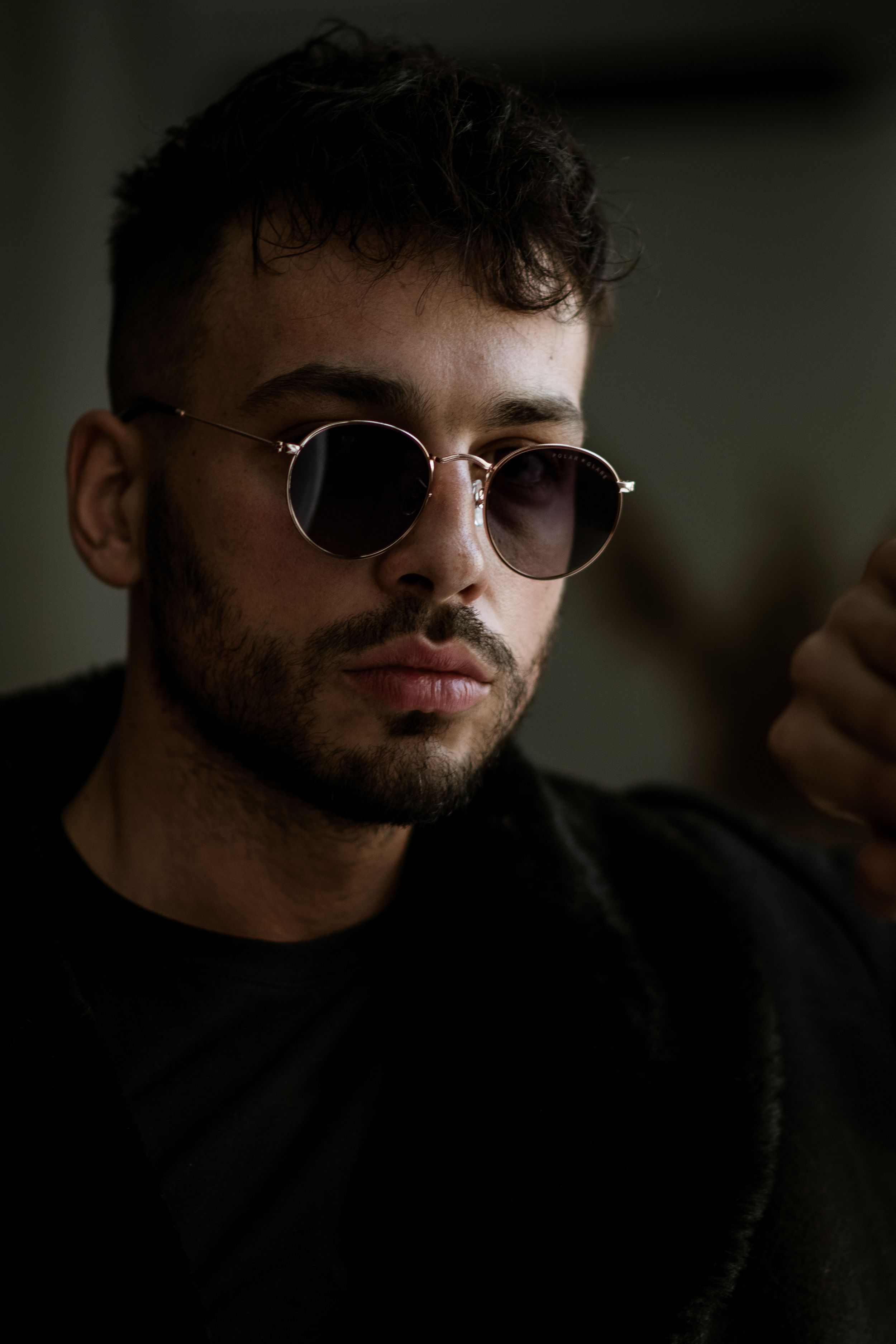 Modern portrait of a person wearing round sunglasses in dark atmospheric lighting.