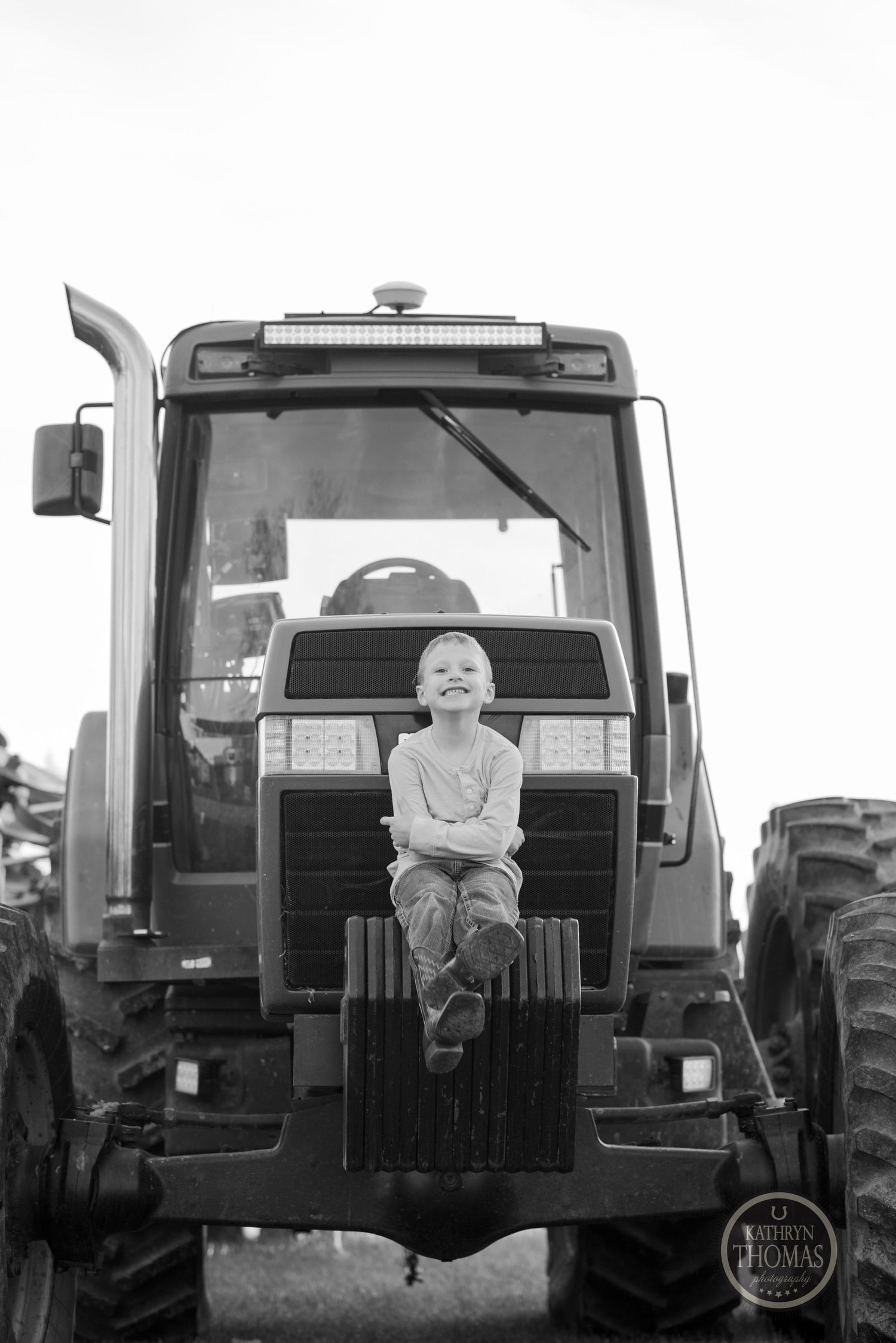 Black and white portrait of a child sitting on the front of a tractor.