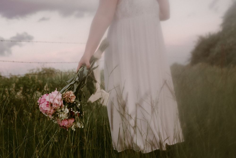 Ethereal shot of flowing white dress and pink bouquet in misty field at dusk.