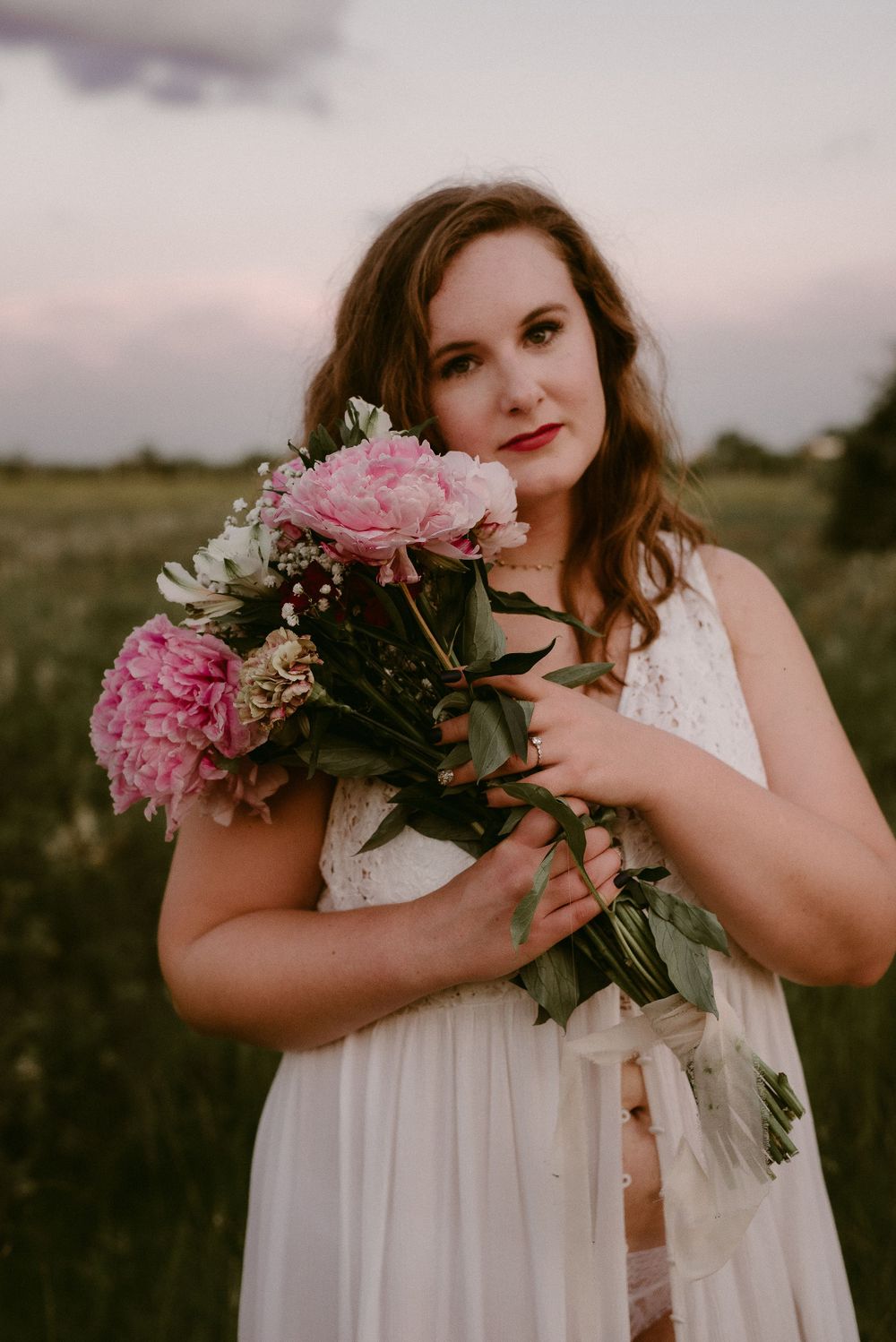 A dreamy portrait with pink peonies and white lace dress in a summer meadow at dusk.