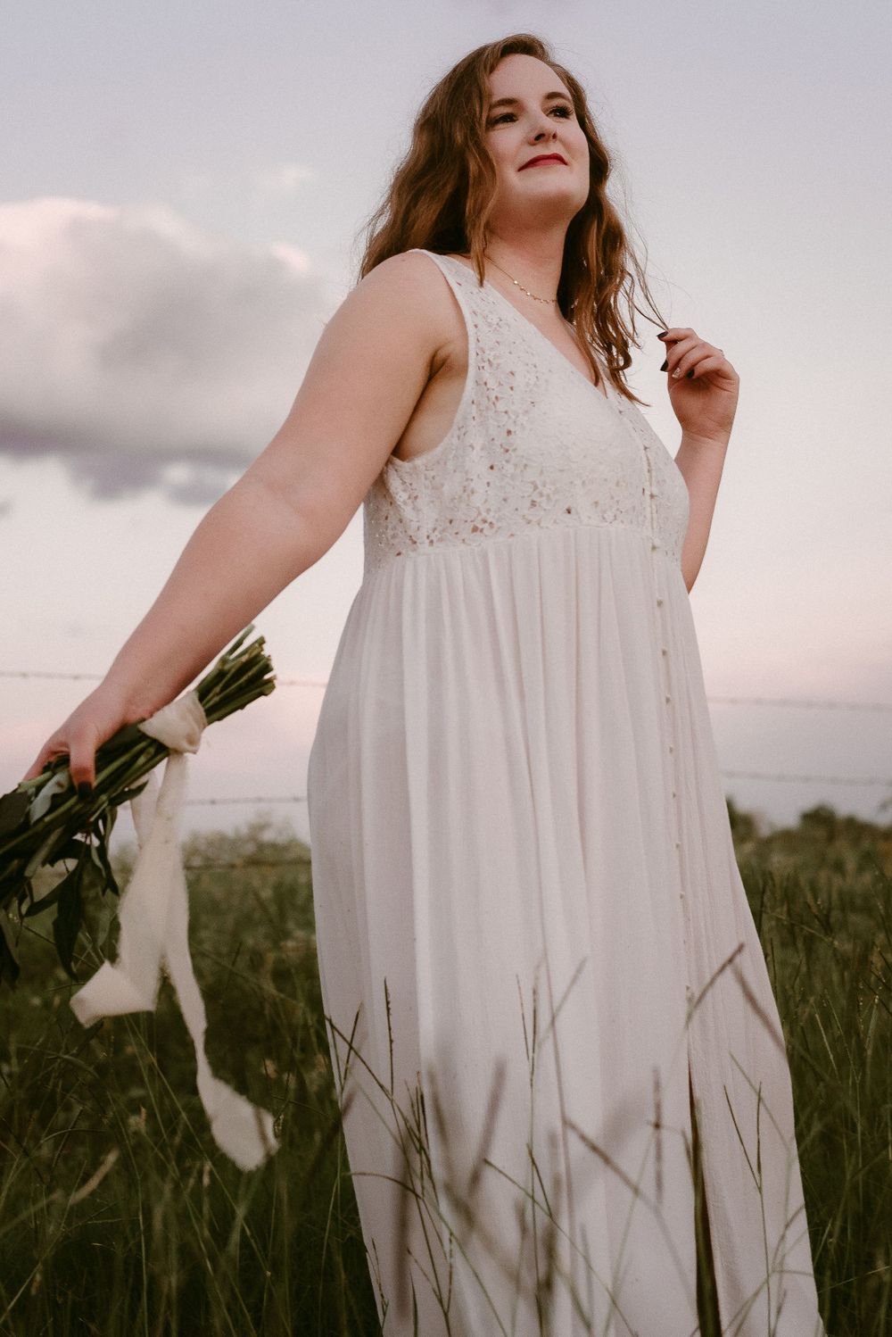 An ethereal white lace dress flows in the breeze while holding flowers at sunset.