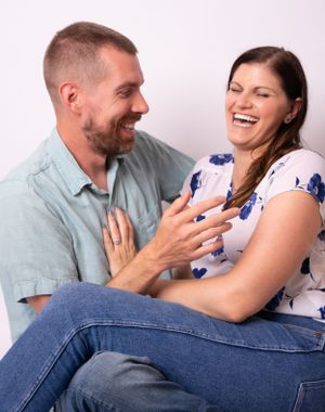 Playful couple in casual wear laughing and embracing on white studio background.