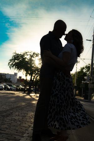 Silhouetted couple embracing at sunset against urban backdrop with cobblestone ground.