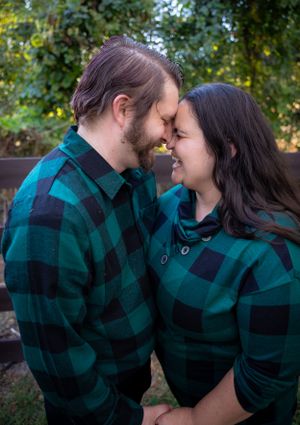 Couple wearing matching teal plaid shirts share romantic moments outdoors among trees.