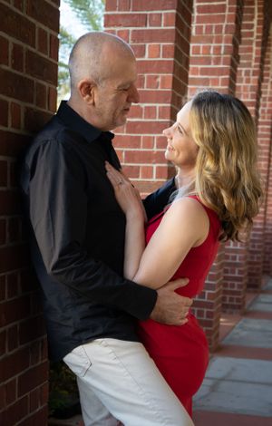 Dancing couple in red dress and black shirt spinning against brick wall backdrop.